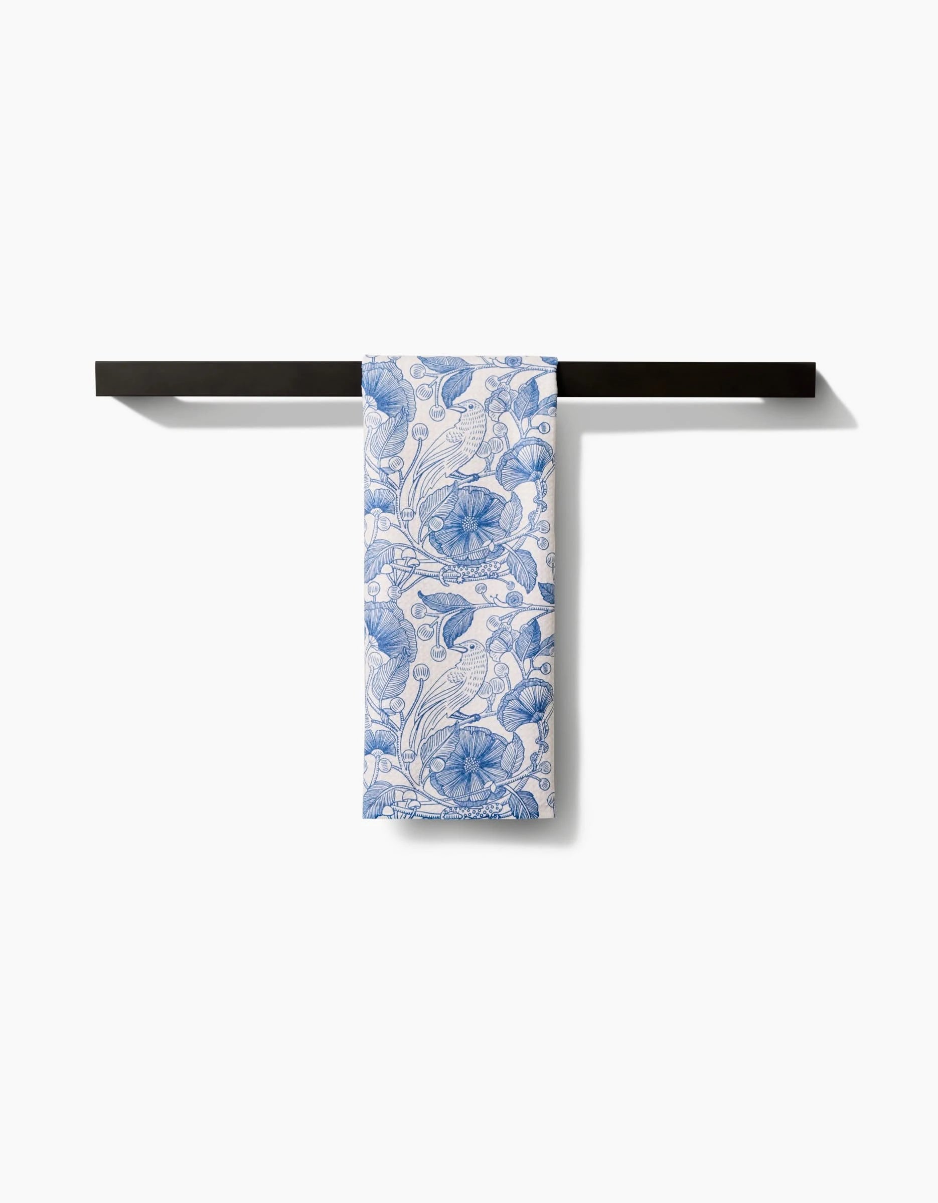 The Katie OShea Crowberries towel, featuring a blue and white floral pattern and made from ultra-absorbent materials, is neatly folded over a simple black rack against a white background.