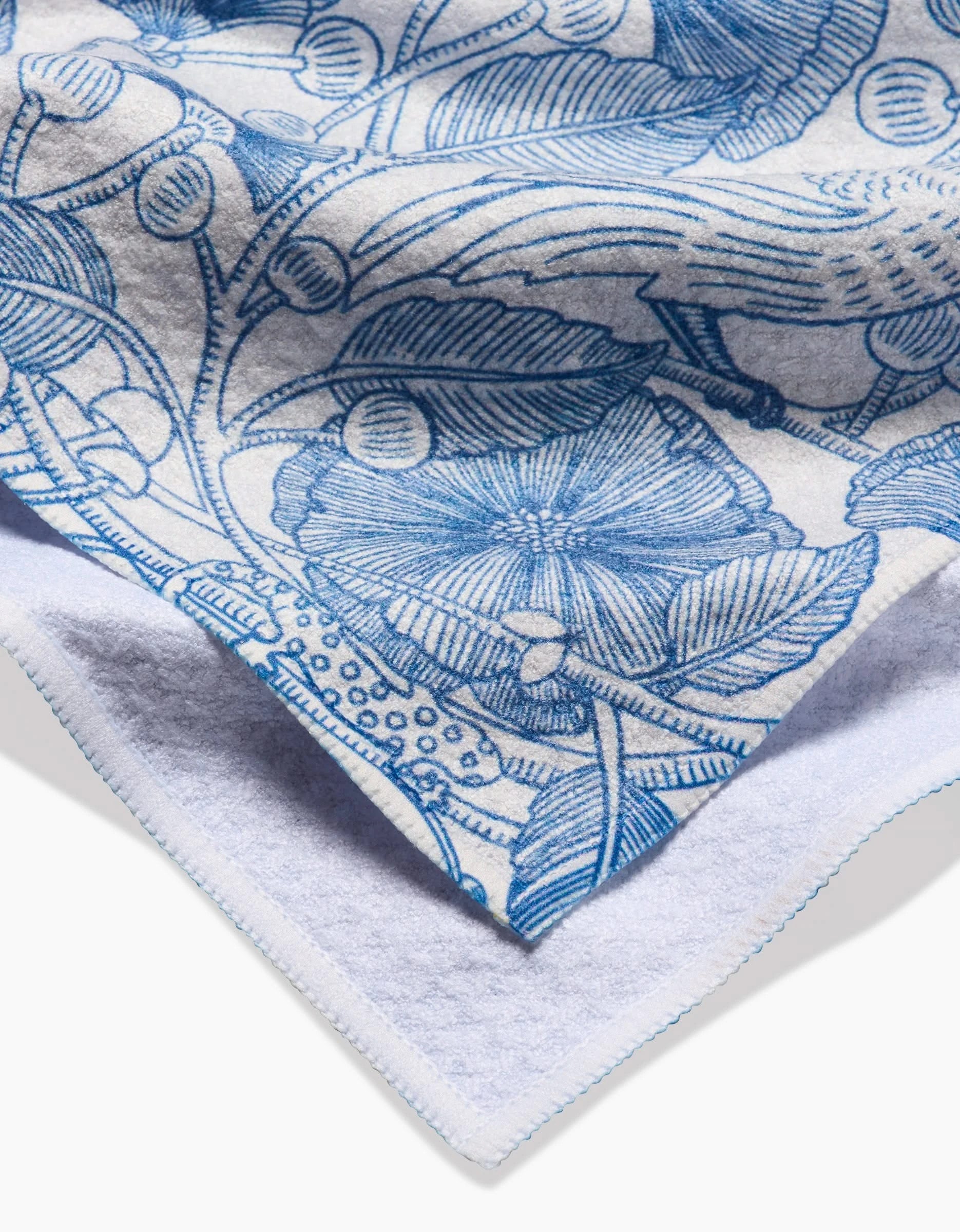 A close-up of the Katie OShea Crowberries Tea Towel shows detailed texture and the edge folded over, featuring an intricate blue floral and leaf pattern on white ultra-absorbent fabric.