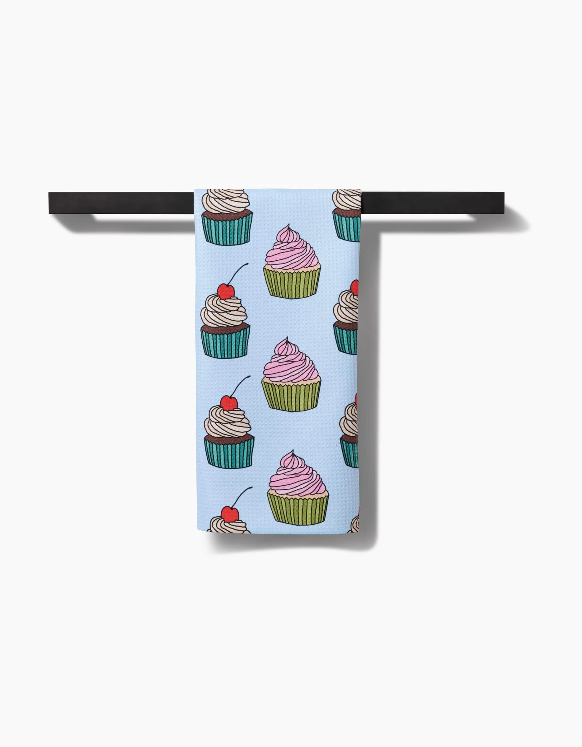 Cupcake Love by Amy Droubay: A light blue tea towel with a colorful cupcake print, made from premium Geoweave fabric, hangs over a black rod against a white background.