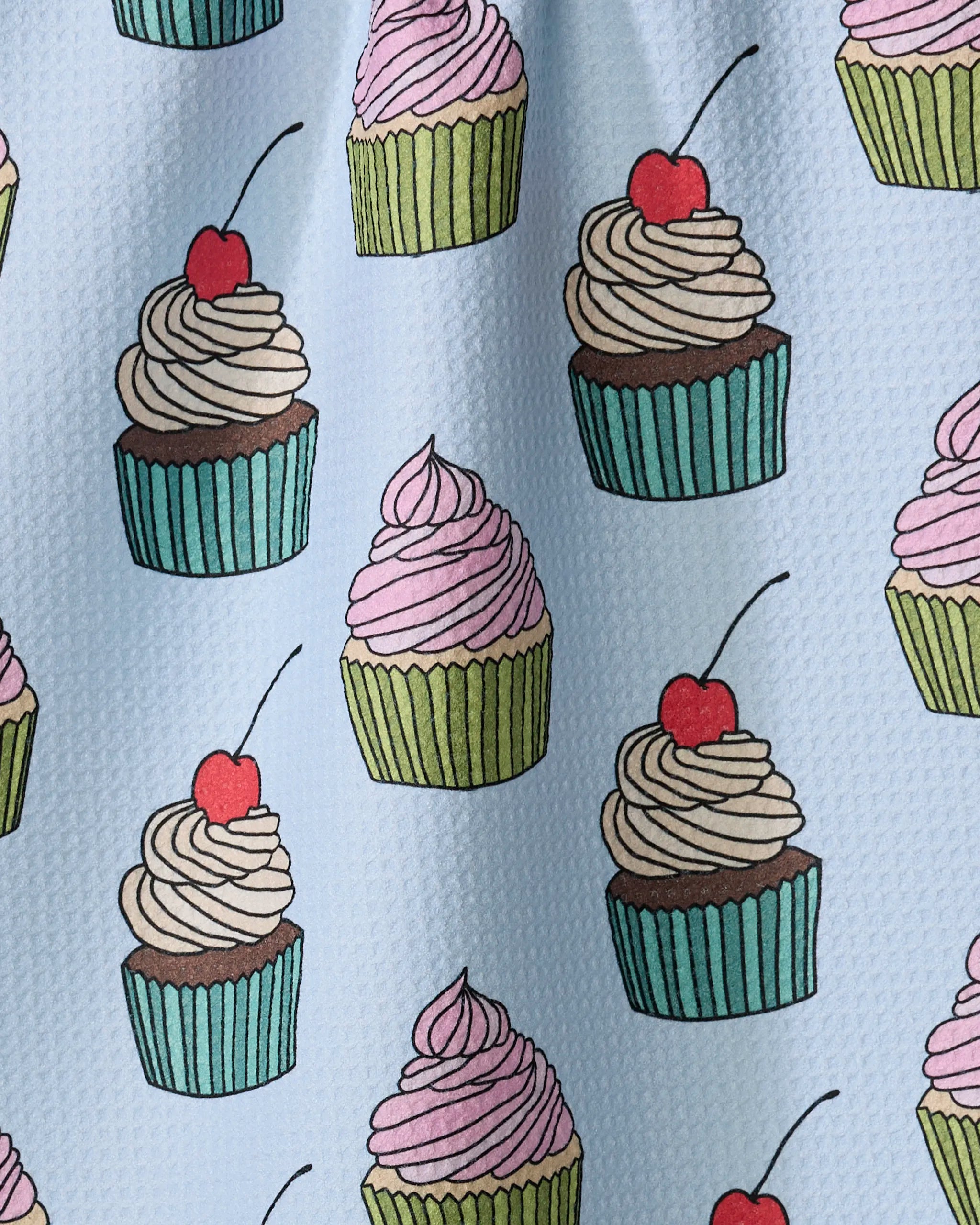 Cupcake Love by Amy Droubay is a light blue Geoweave tea towel featuring a repeating pattern of colorful cupcakes in green or blue liners, topped with pink or white frosting and cherries.