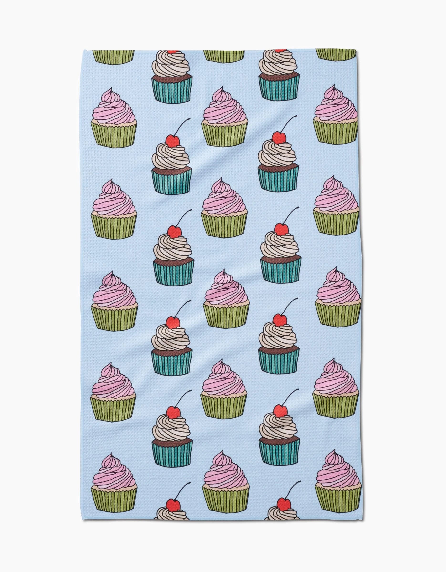 Cupcake Love by Amy Droubay is a light blue tea towel made from recycled materials, adorned with colorful cupcakes—featuring pink or white frosting, green or blue wrappers, red cherries on top, and a single cherry near the bottom edge.