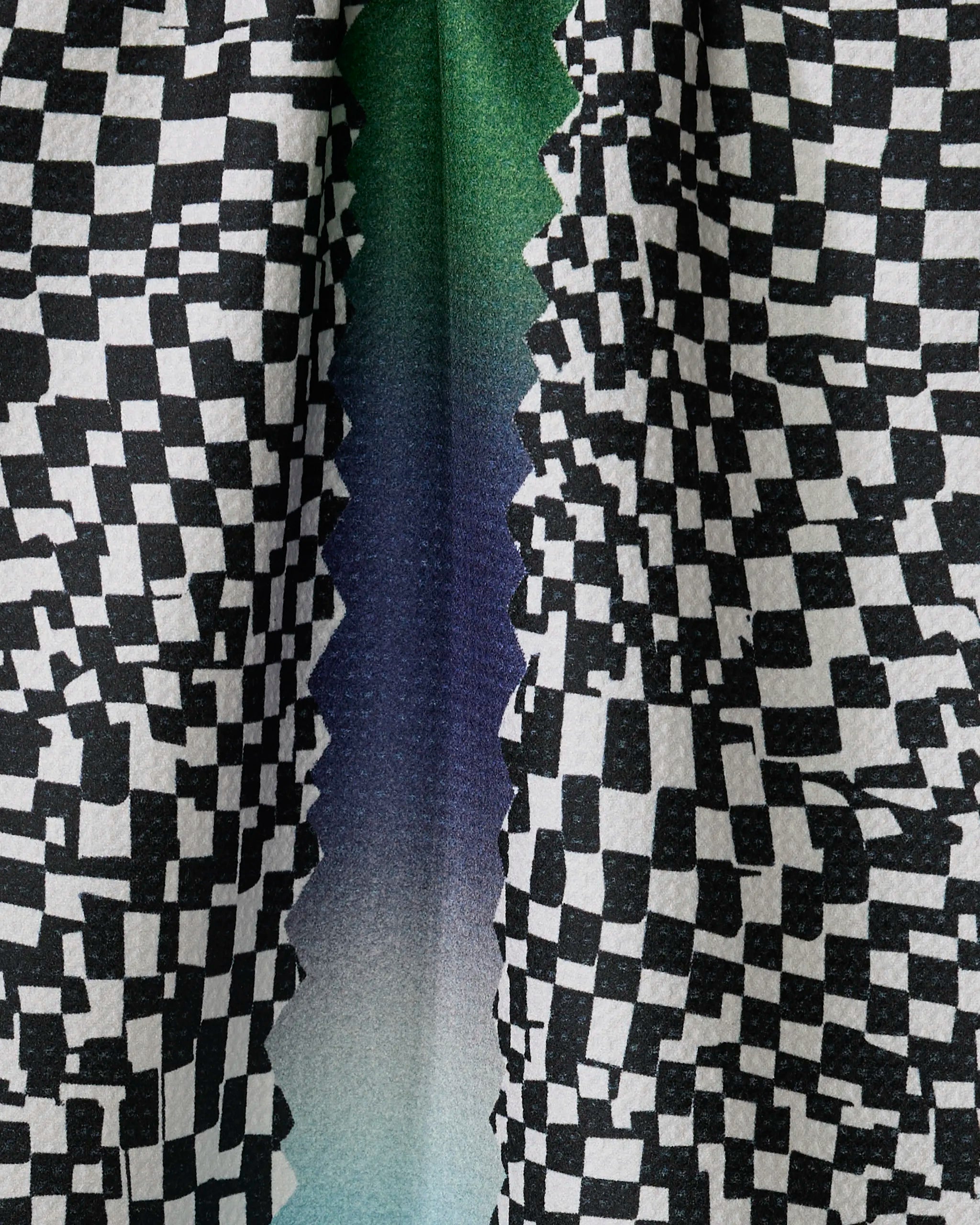 Close-up of Geometry’s “Current” tea towel with a black and white checkered pattern, jagged zigzag edge, and a green-to-blue-to-purple gradient. Made from quick-drying, recycled materials for eco-friendly use.