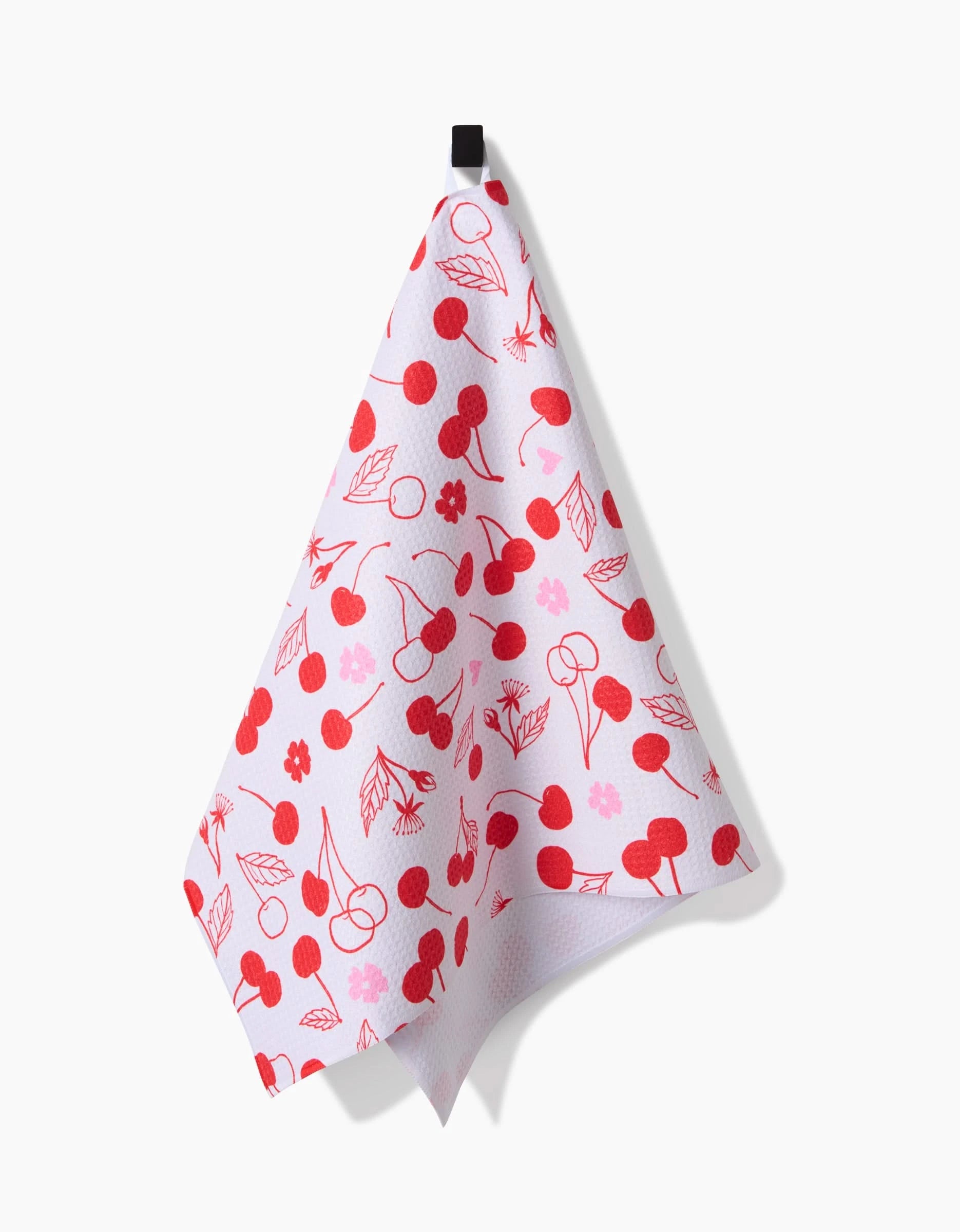 The Elana Gabrielle Cute Cherry white tea towel, featuring a red cherry and leaf pattern, hangs from a black hook against a plain white background.