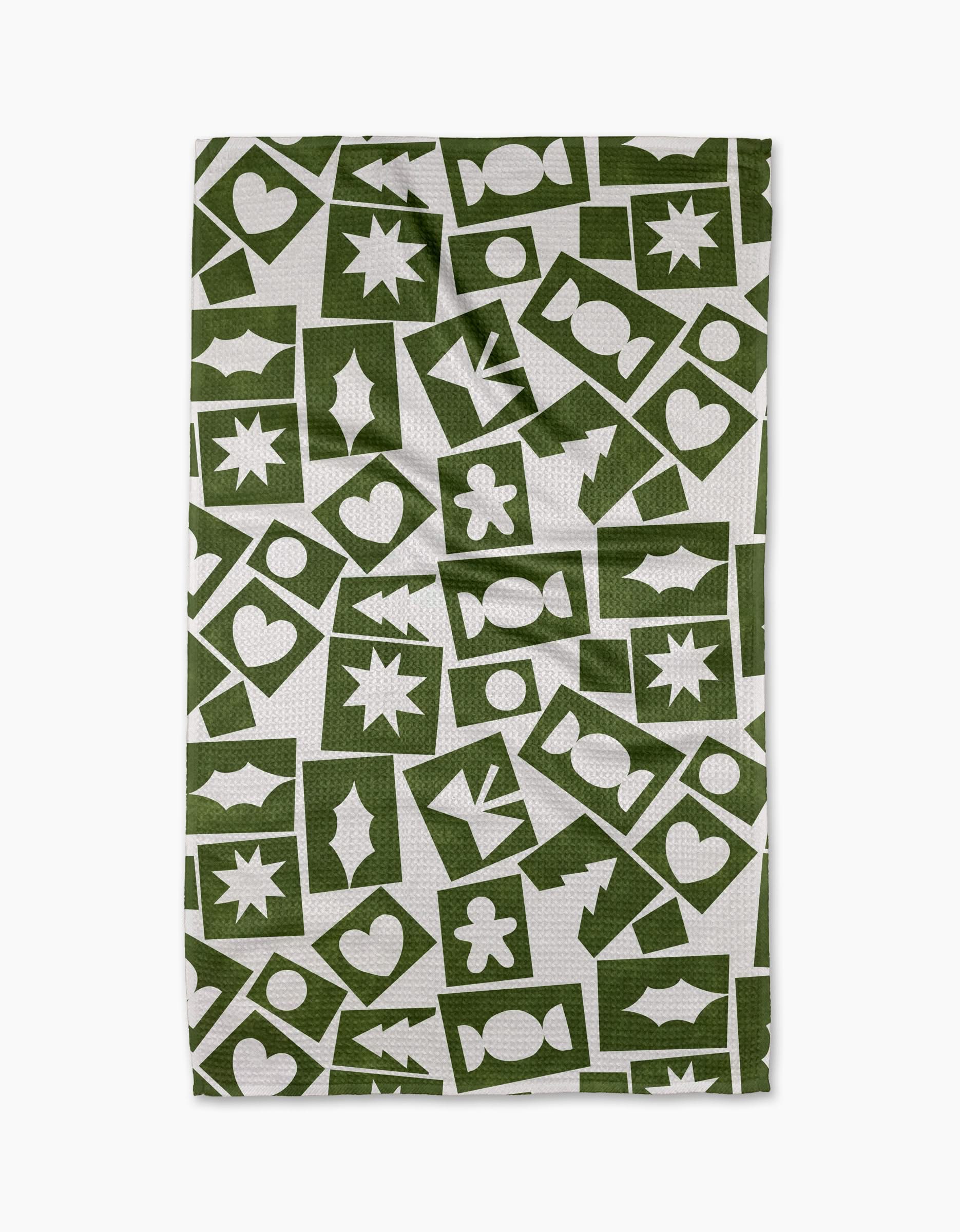 The Cutout Christmas tea towel by Claire Iglesias is a white recycled kitchen towel featuring green hearts, stars, circles, and holiday shapes in a stylish grid pattern—an eco-friendly and festive addition to your home.