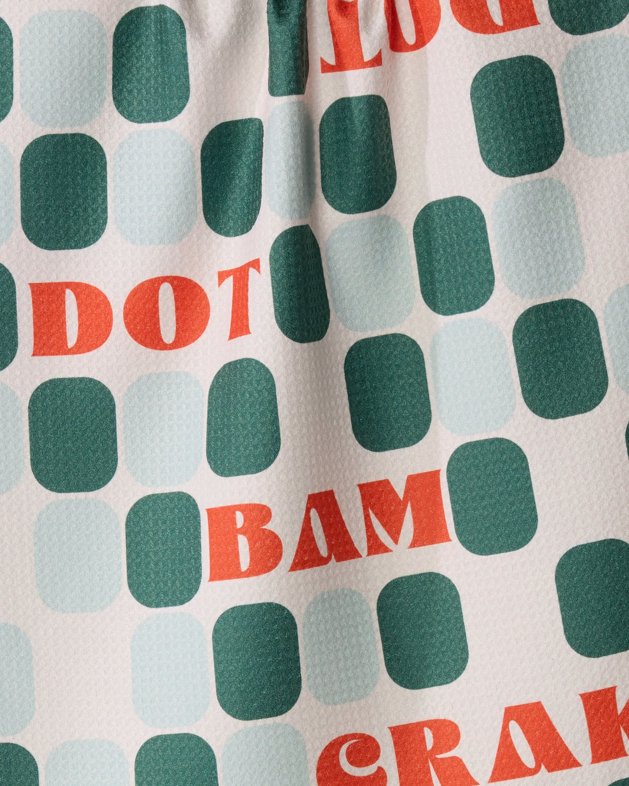 The Geometry Cypress Tile Talk Tea Towel features a vibrant design of green and light blue squares on textured white Geoweave fabric, boldly displaying red letters that spell “DOT,” “BAM,” and partial words. Crafted from recycled materials, this eco-friendly towel combines eye-catching style with sustainable functionality.