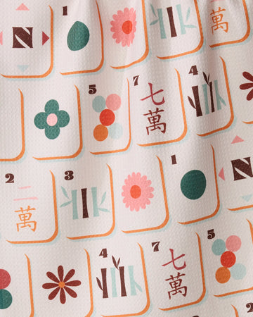 The Cypress Tile Toss kitchen towel by Geometry features vibrant symbols, numbers, and Chinese characters inspired by mahjong tiles, printed on textured white fabric made from recycled materials. With playful flowers, circles, and bamboo patterns in pink, green, orange, and teal hues, this ultra-absorbent tea towel is perfect for adding a unique touch to your kitchen.