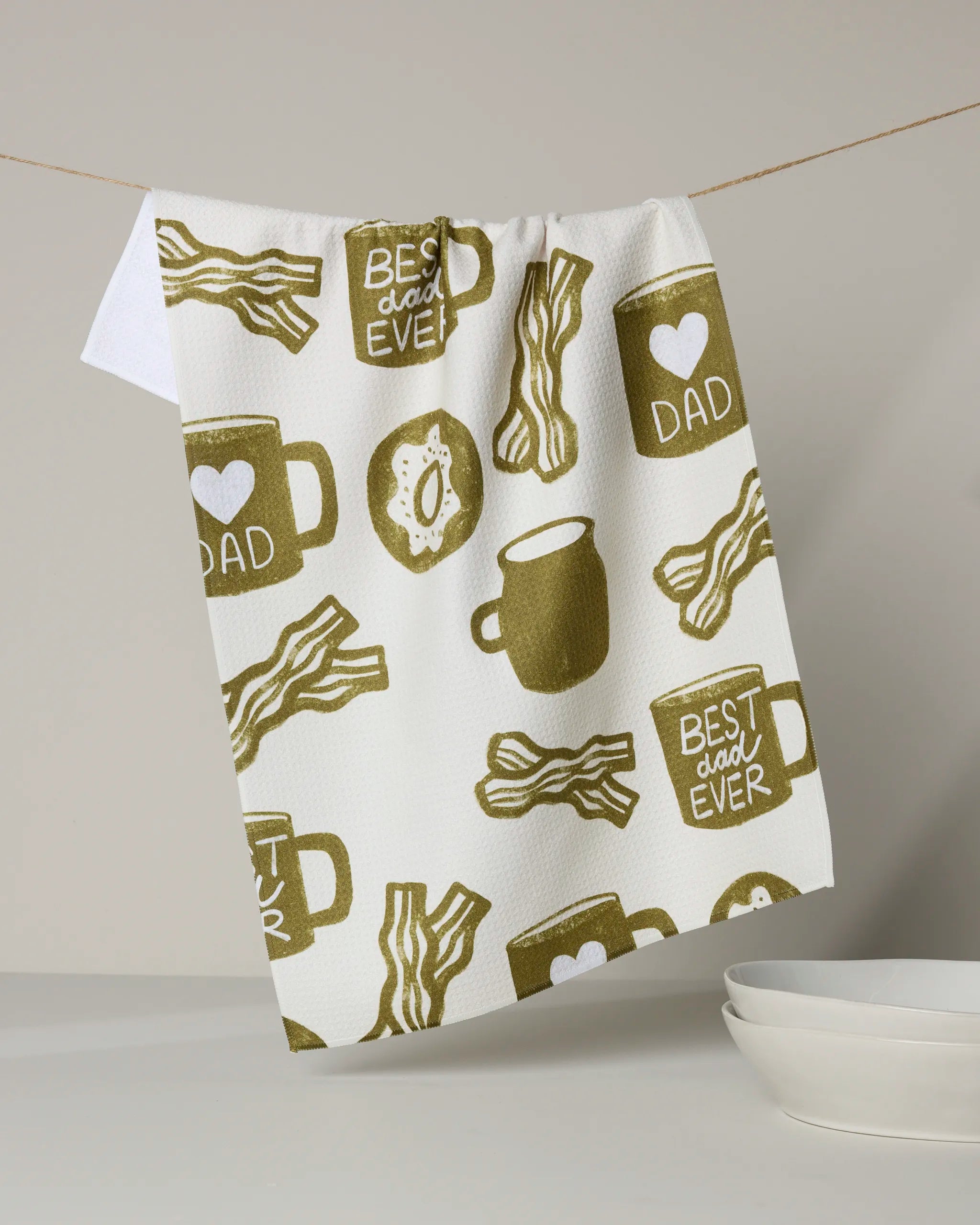 The "Dad Fuel" kitchen tea towel by Lisa Nelson showcases olive green illustrations of bacon, coffee mugs labeled DAD and BEST DAD EVER, and an egg over stacked bowls. Made from recycled materials for eco-friendly use.