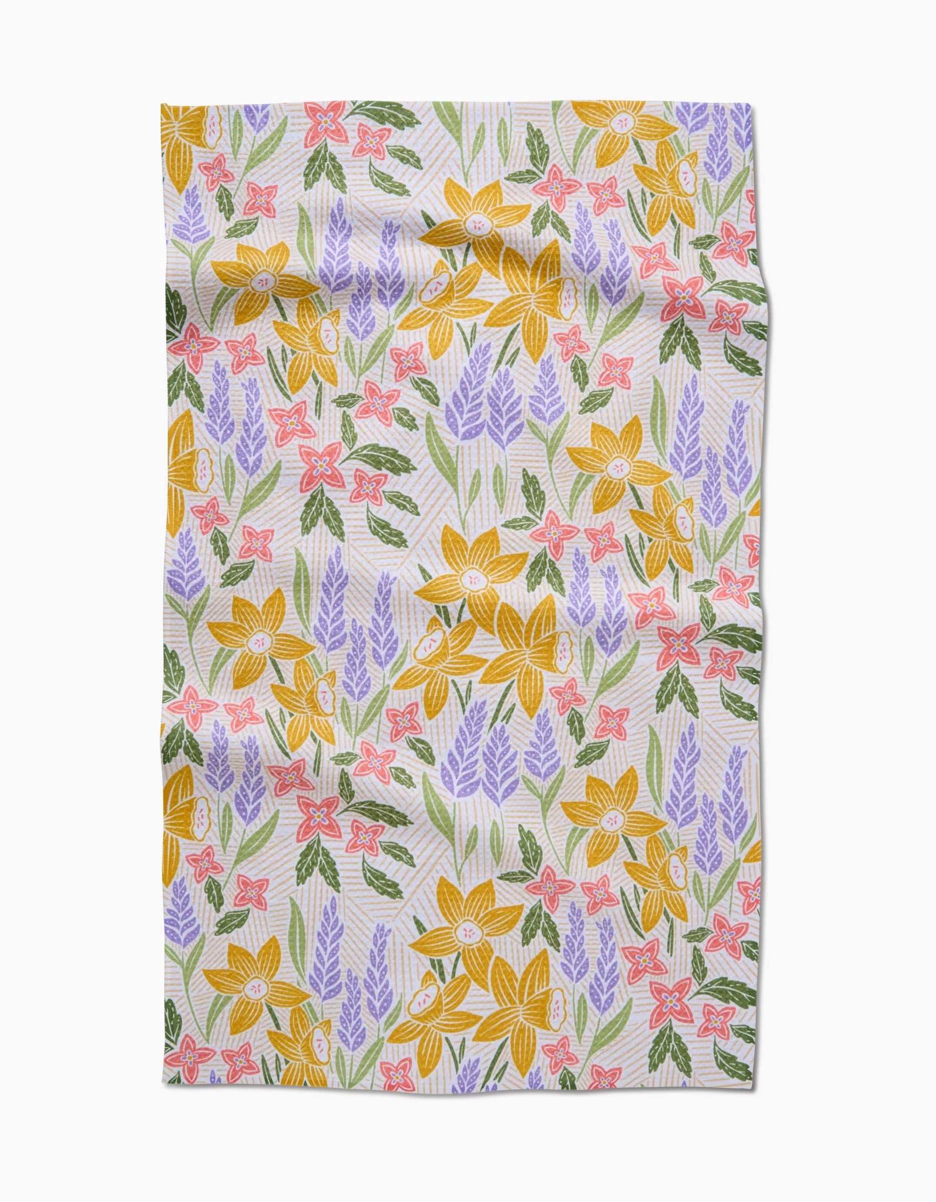 The Daffodil Dreams tea towel by Sarah Daugherty features a rectangular design with large yellow flowers, purple and pink blooms, and green leaves on a light background. The Geoweave fabric has a slightly wrinkled appearance.