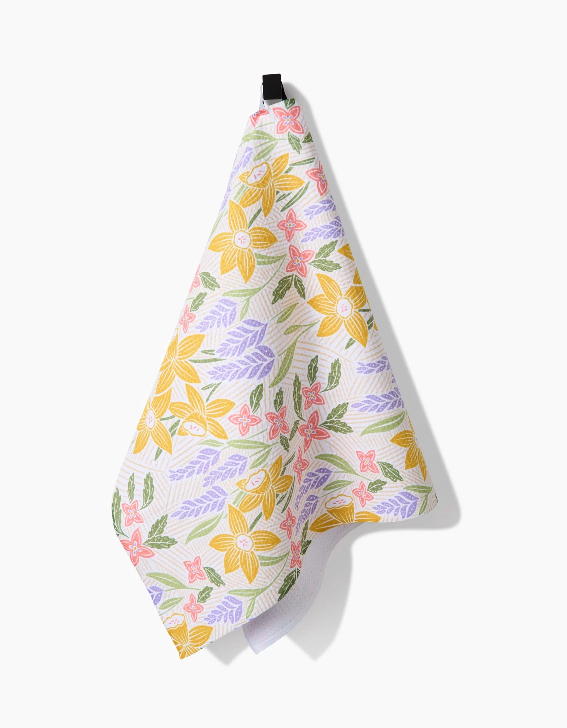 The Daffodil Dreams tea towel by Sarah Daugherty features yellow flowers with pink, purple, and green accents. Made from recycled materials, it hangs from a black loop and is shown on a white background.
