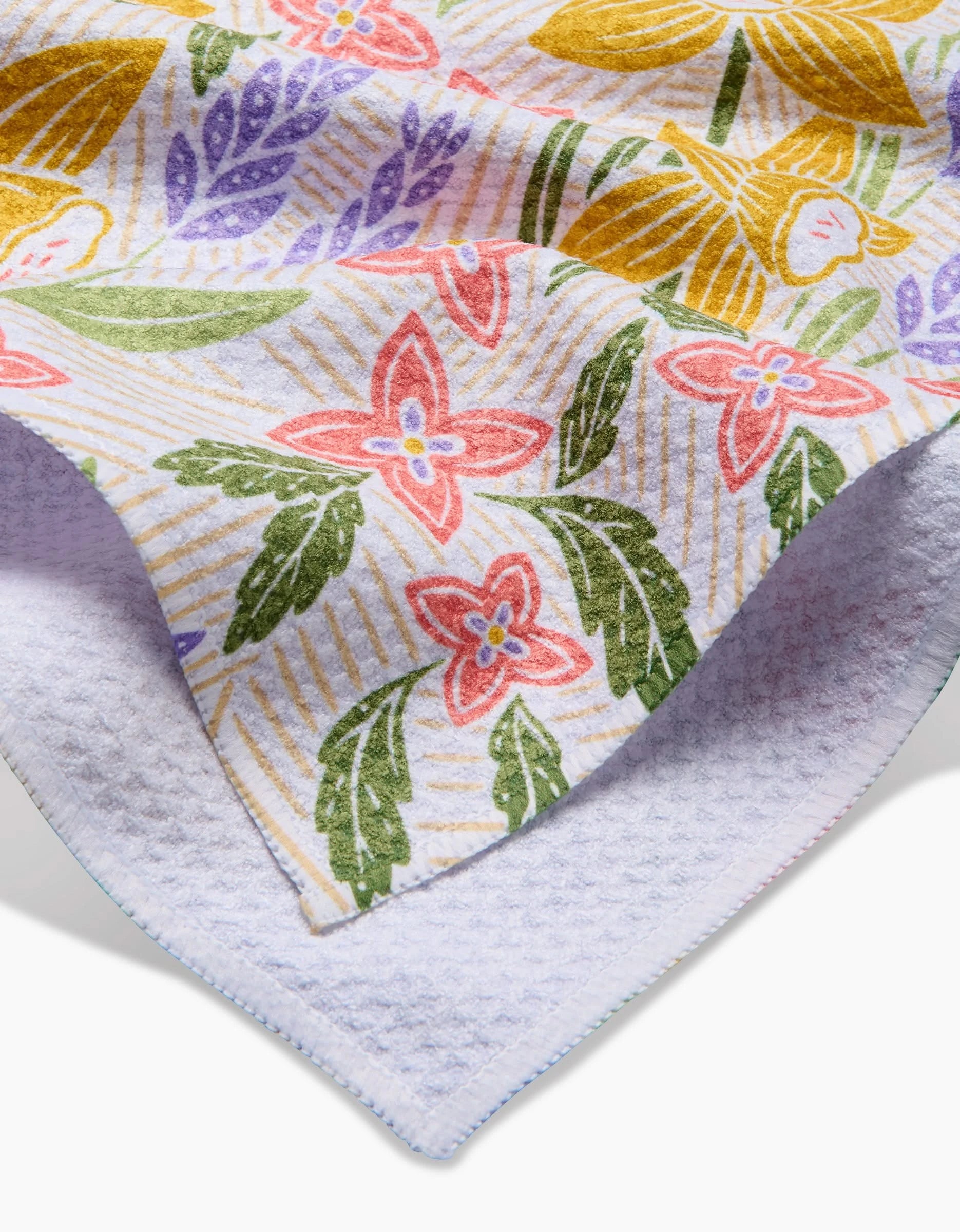 A close-up of the Daffodil Dreams tea towel by Sarah Daugherty, showing its colorful floral pattern and folded corner that reveals the soft Geoweave fabric underside.