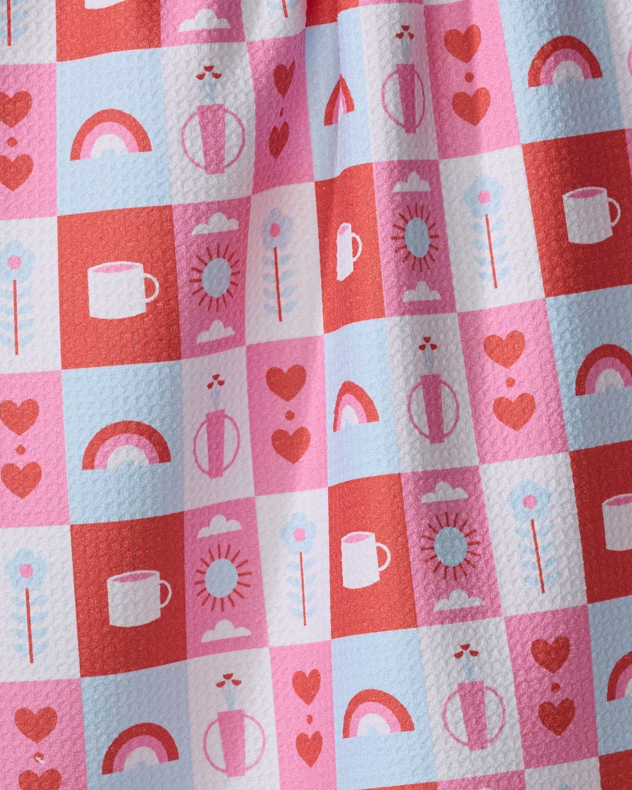 Daily Icons" by Laura Supnik is a recycled kitchen towel with a textured checkered pattern in pink, red, and blue, featuring hearts, rainbows, suns, coffee cups, arrows, and flowers.