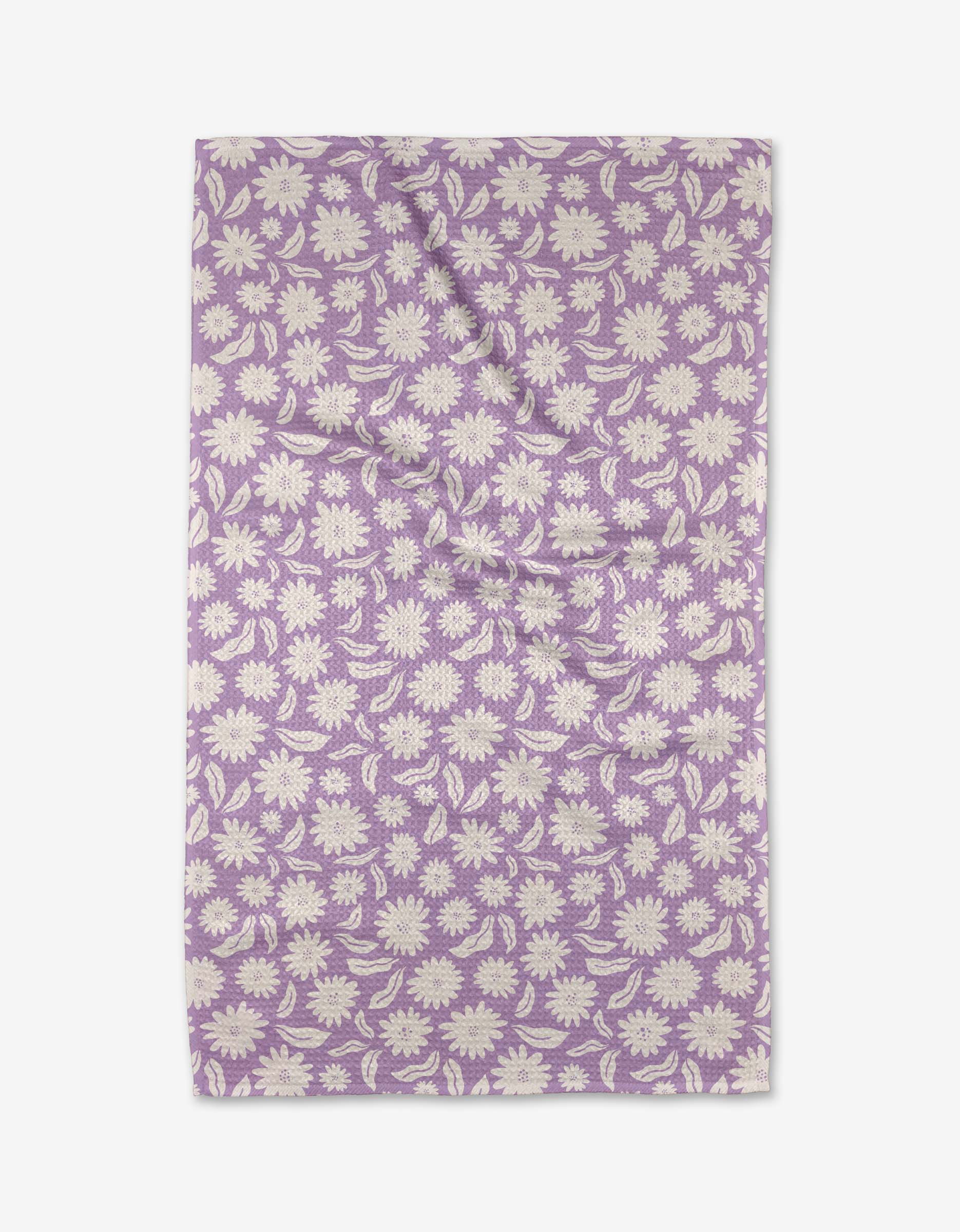The Kayla Ann Daisy Bloom rectangular tea towel is made from recycled materials and features a lavender base with a white daisy and leaf pattern, shown laid flat with slight wrinkles.