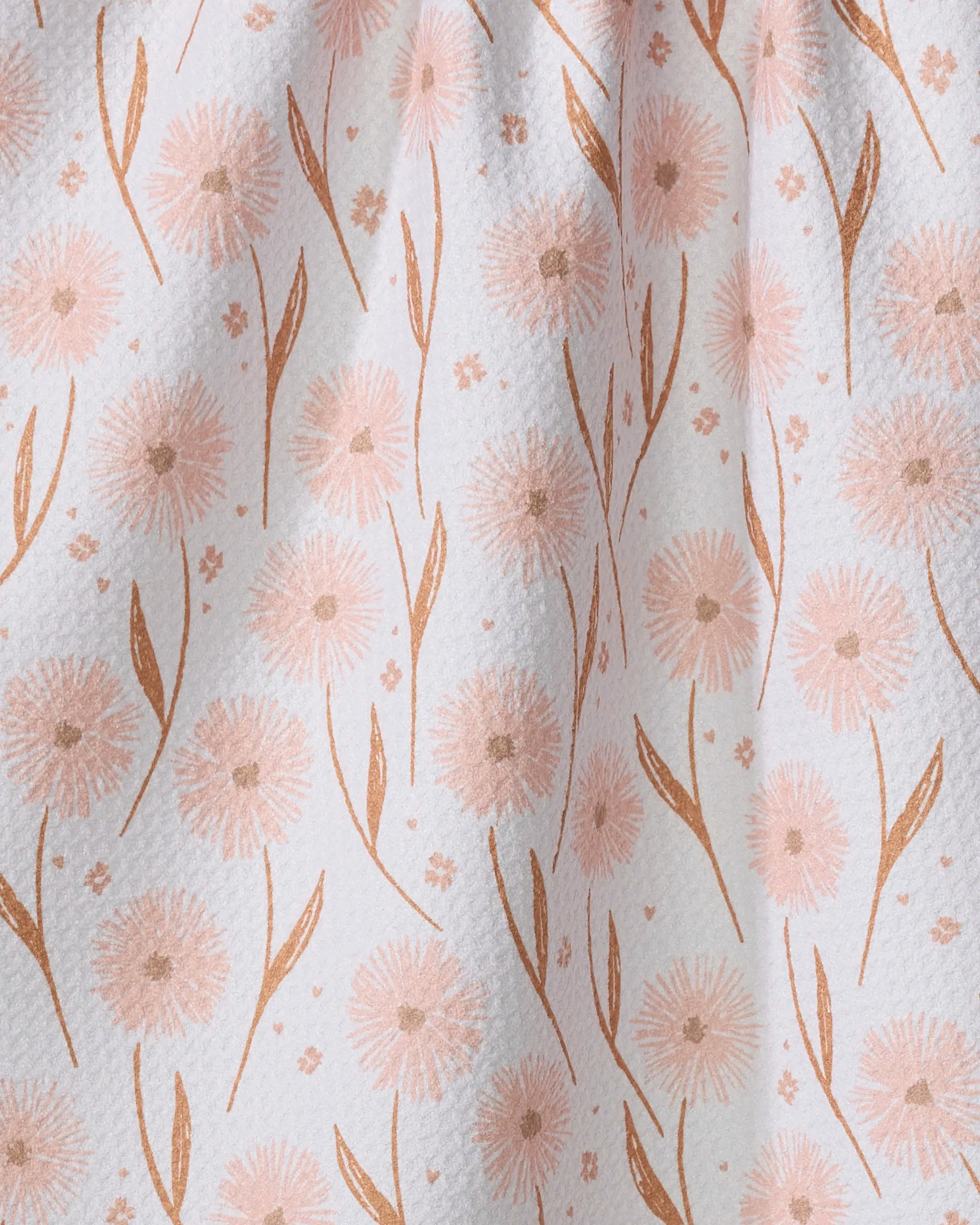 Close-up of the Hufton Studio Daisy Pop tea towel featuring a delicate pattern of light pink dandelion-like flowers and curved leaves on softly draped, textured white Geoweave fabric.