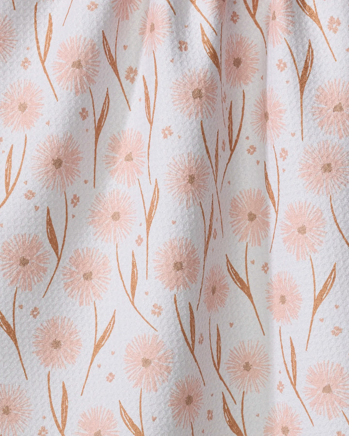 Close-up of the Hufton Studio Daisy Pop tea towel featuring a delicate pattern of light pink dandelion-like flowers and curved leaves on softly draped, textured white Geoweave fabric.