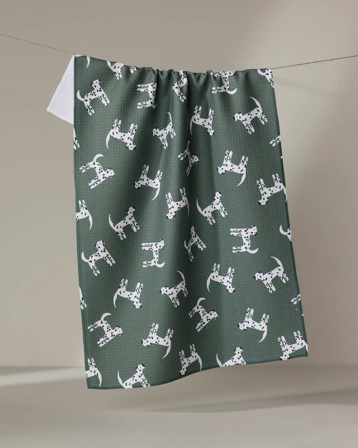 The Coit Creative "Dalmatian Dogs" ultra-absorbent green tea towel, featuring a repeating white Dalmatian pattern, is shown hanging on a clothesline against a neutral background.