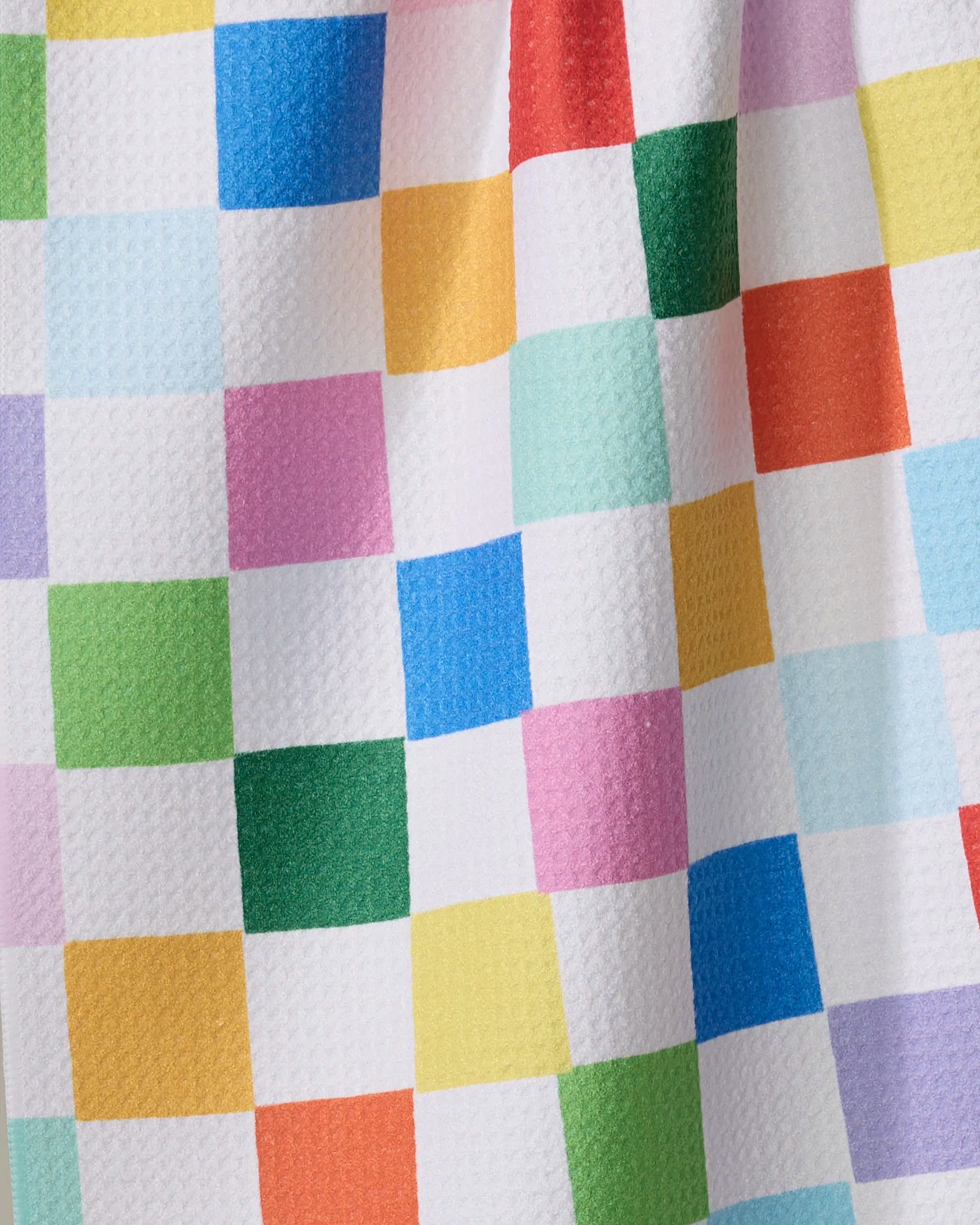 A close-up of the "Dance Floor" tea towel by Vaishali Design Studio, showing its colorful checkered pattern in green, blue, pink, yellow, red, and white. The textured absorbent fabric features small squares and a slightly wavy appearance.
