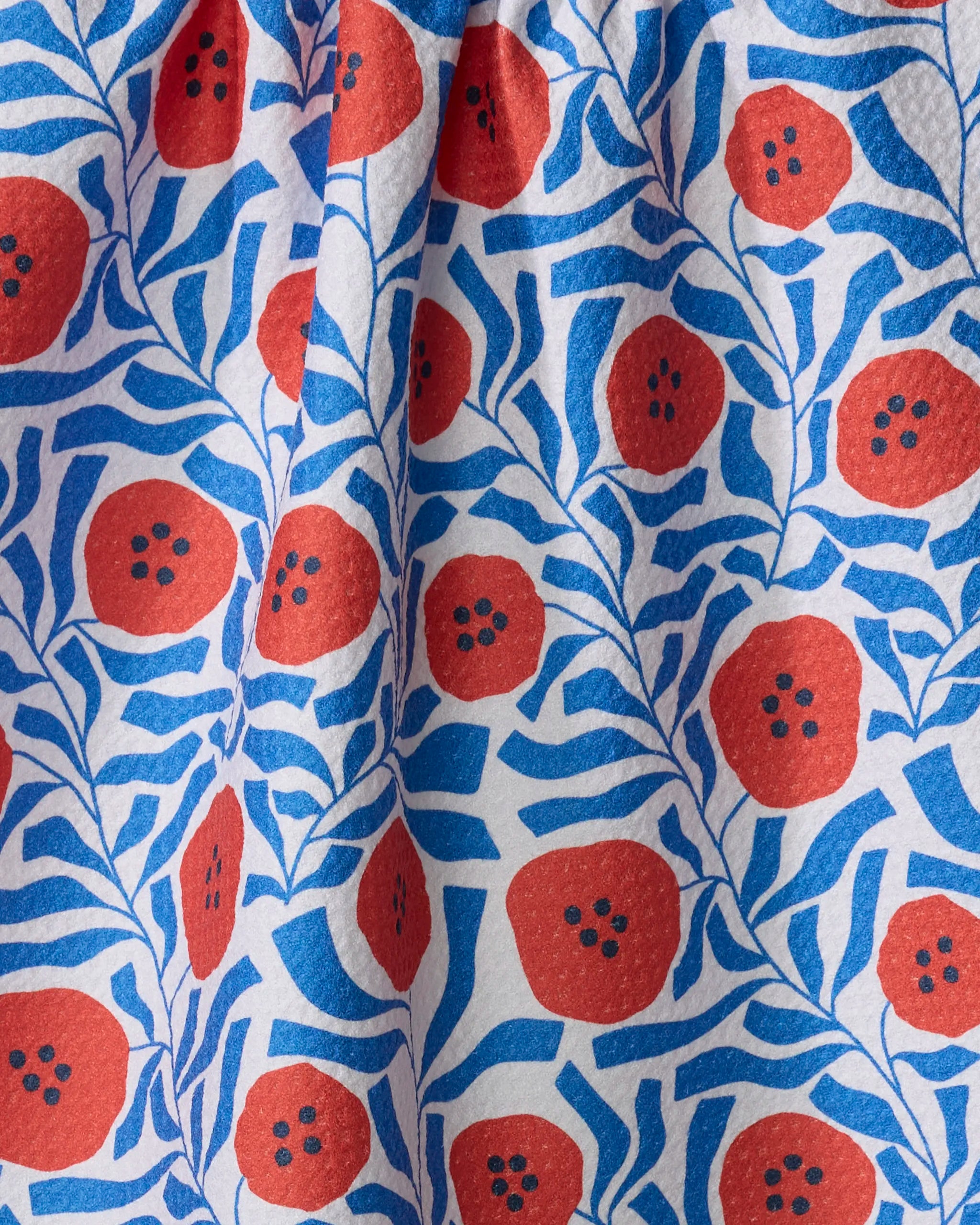 The Dancing Poppies tea towel by Happy Hemera features a bold red flower and blue leaf pattern on white, made from recycled materials. Its vibrant, densely packed design is quick-drying and slightly wrinkled for added charm.