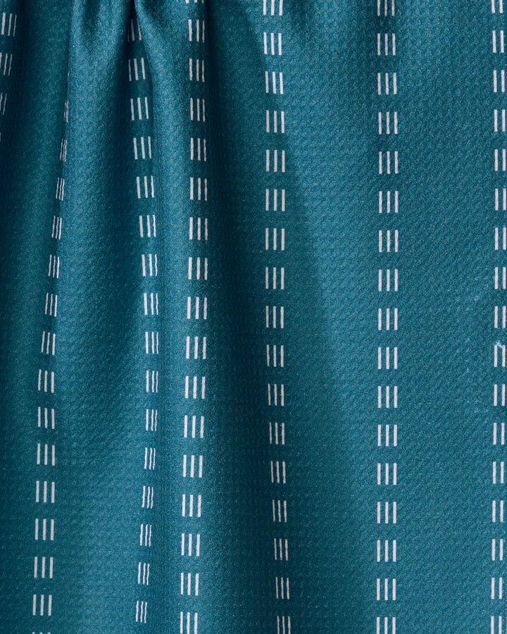 Close-up of Dashing - Emerald by The Buy Guide: a teal kitchen towel crafted from recycled materials, featuring vertical rows of evenly spaced white dashed lines in a simple, modern pattern and slightly gathered fabric at the top.