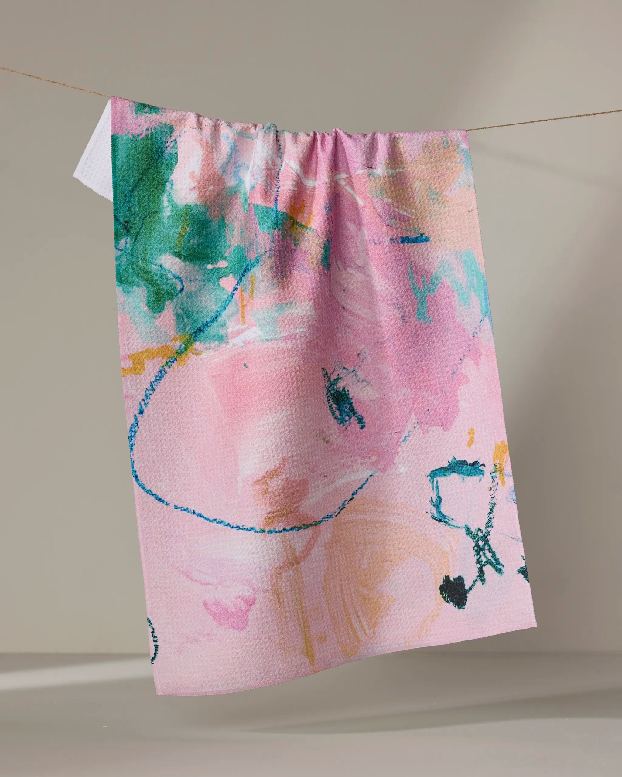 The Sarah Holden "Daughter" tea towel, featuring a vibrant abstract design in pink, green, blue, orange, and black, hangs on a clothesline against a neutral background.