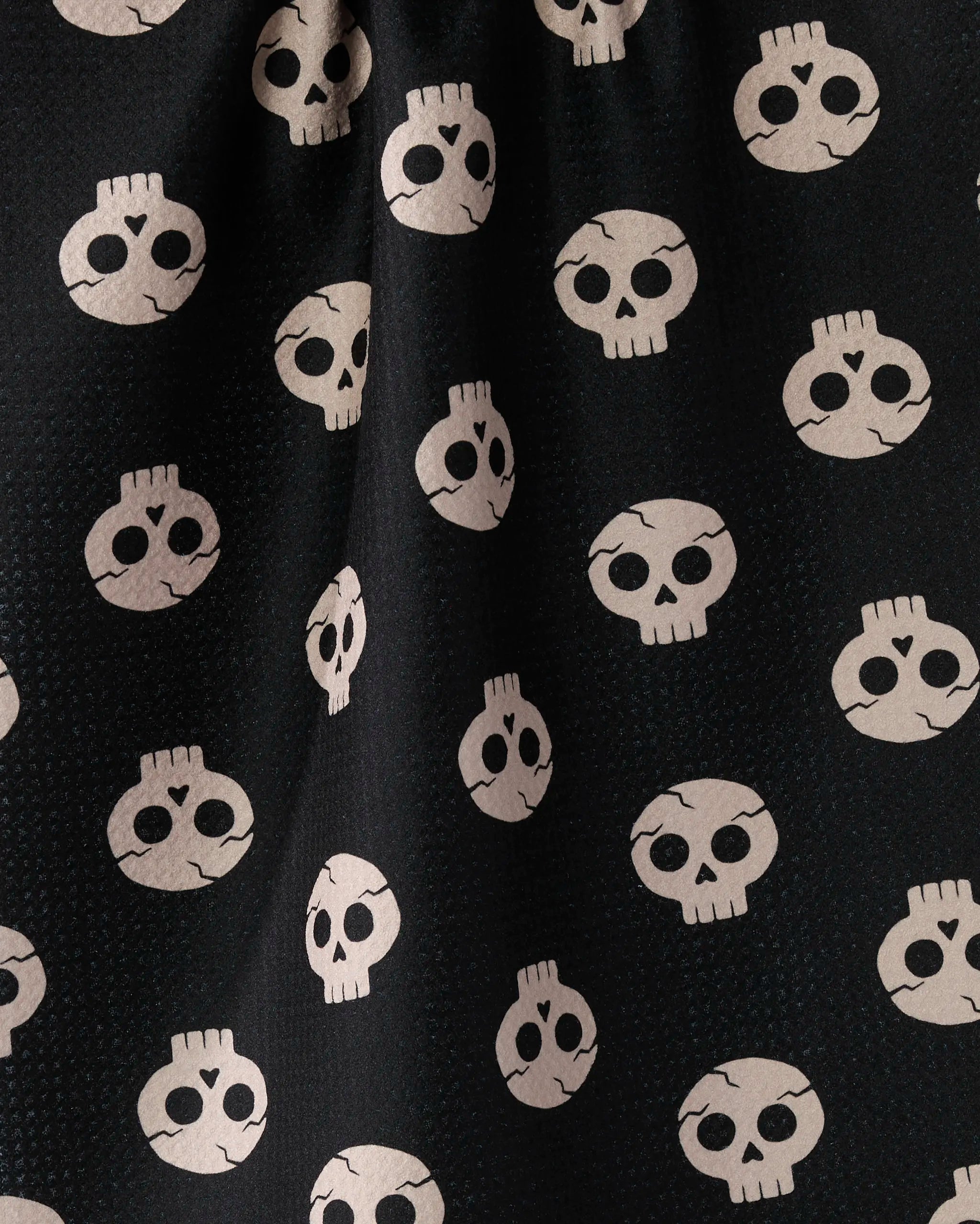 The Dead Cute tea towel by Geometry features black fabric with white cartoon skulls, each showing big round eye sockets. Made from recycled materials, this ultra-absorbent towel is slightly gathered for added texture and style.