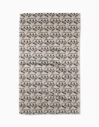 Cole Strems “Dead Set” is a beige rectangular rug with a black repeating pattern of two stylized skeletons side by side in heart shapes, inspired by the geometric designs from the Geometry Tea Towel collection.