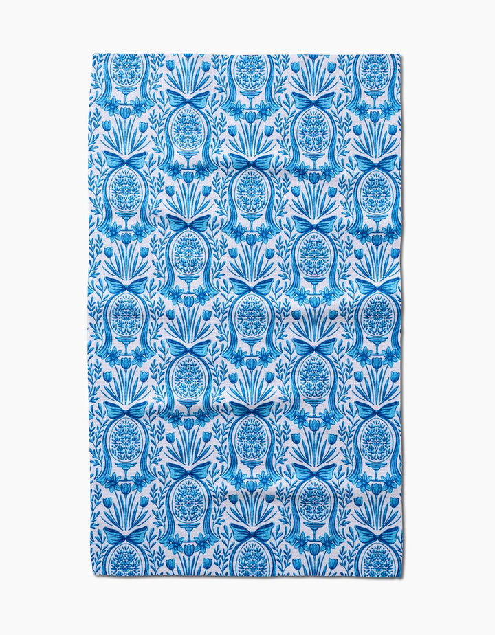 The Sarah Daugherty Delft Blue Easter Egg Damask tea towel features a repeating blue floral and fruit vase pattern with symmetrical, intricate detailing on a white background.