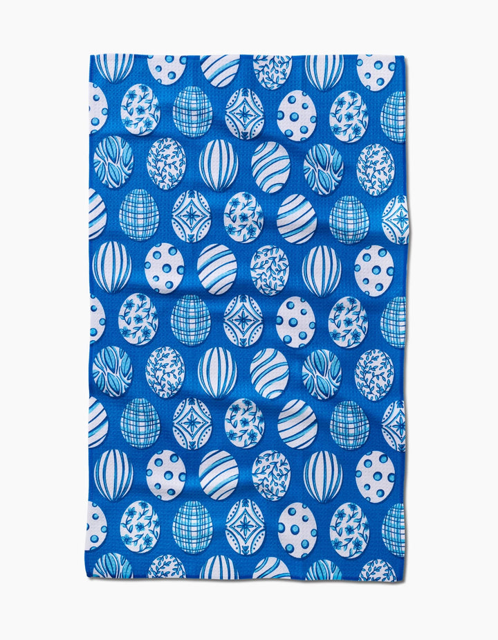 The Delft Blue Easter Eggs tea towel by Sarah Daugherty is rectangular, blue, and made from recycled materials, featuring a repeating pattern of white and blue spheres with geometric and abstract designs.