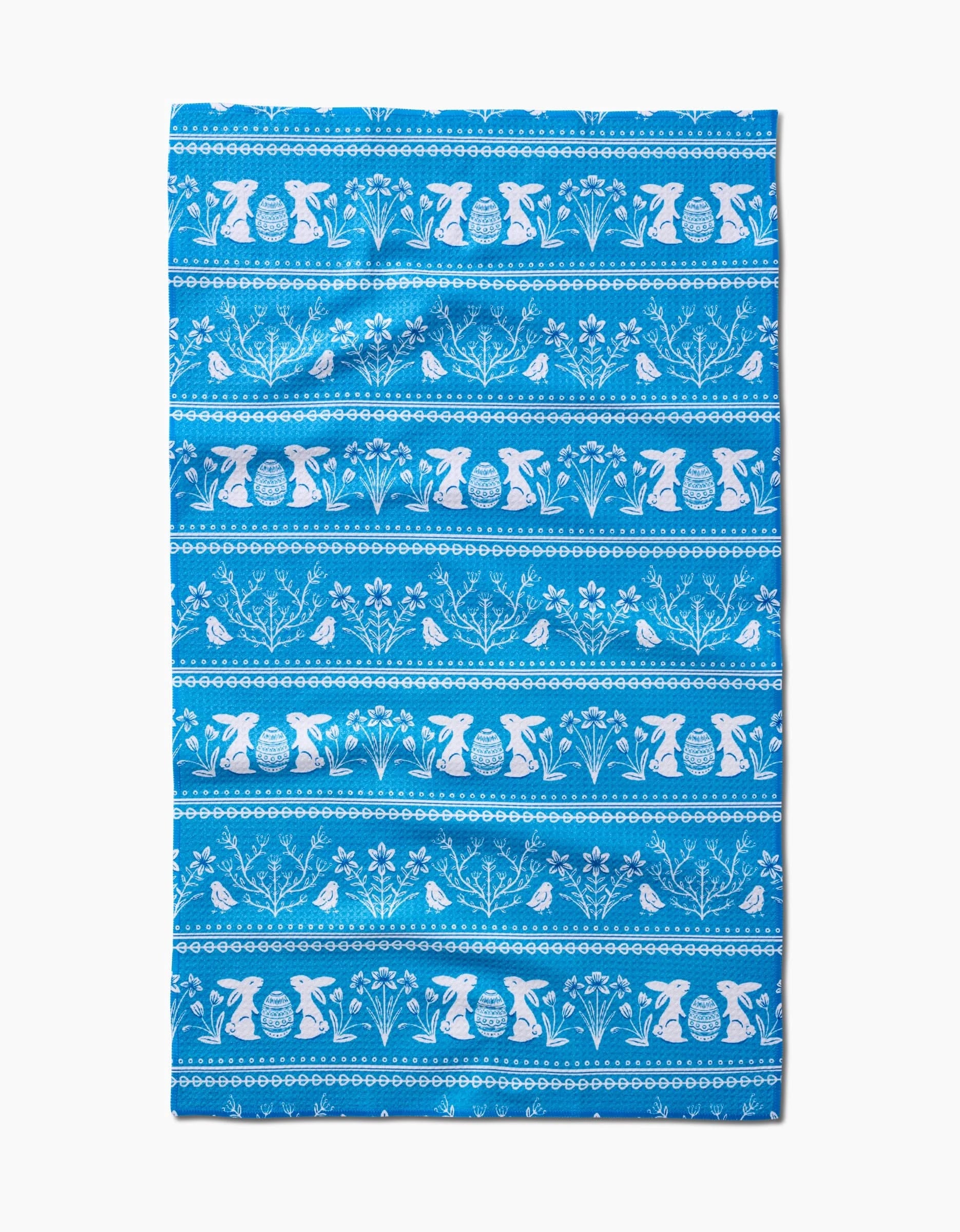 The Delft Blue Easter Stripe towel by Sarah Daugherty is quick-drying and features white horizontal patterns of bunnies, birds, flowers, and decorated eggs in repeating rows on a blue background.