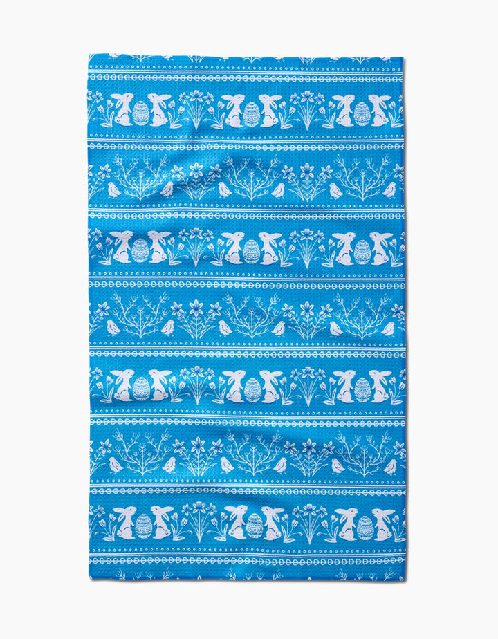 The Delft Blue Easter Stripe towel by Sarah Daugherty is quick-drying and features white horizontal patterns of bunnies, birds, flowers, and decorated eggs in repeating rows on a blue background.