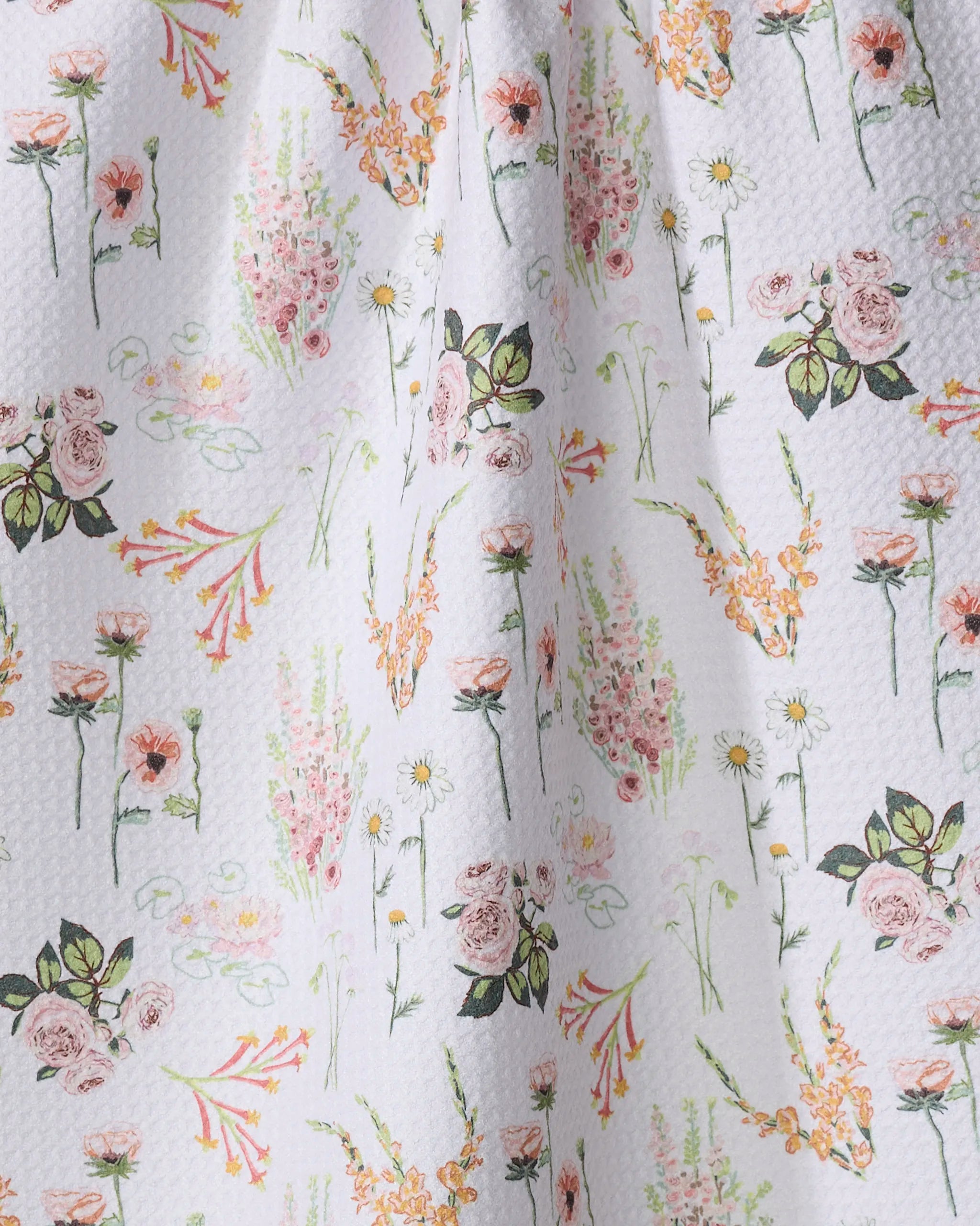 A close-up of the Elisabeth Wing Delicate Floral kitchen towel, showcasing a white textured fabric with a colorful print of roses, daisies, and greenery in pink, yellow, and orange arranged in a delicate scattered pattern.