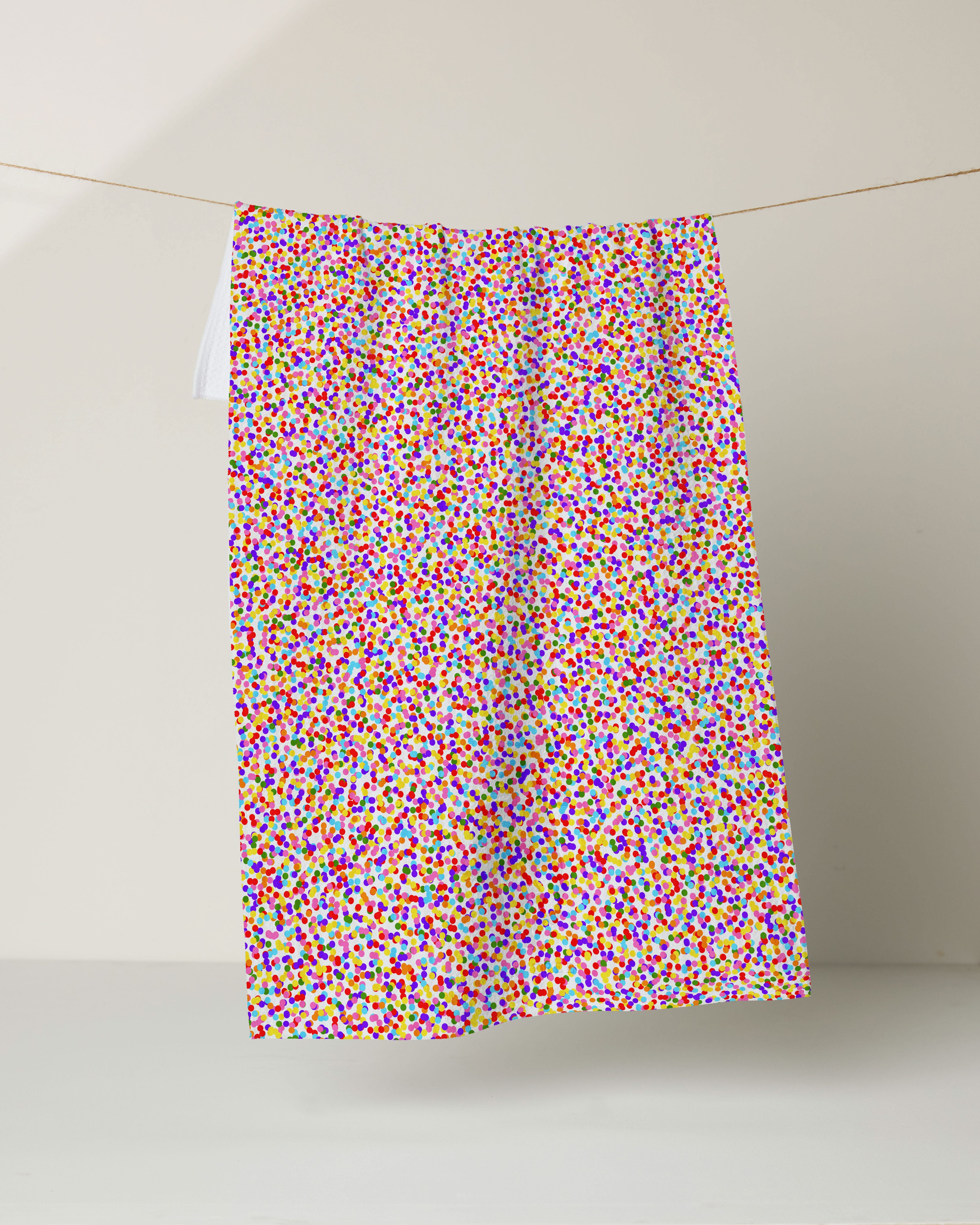 The Deluxe Dot Cake by Geometry, a vibrant fabric made from recycled materials and featuring a dense, multicolored confetti pattern, hangs on a clothesline against a neutral background.