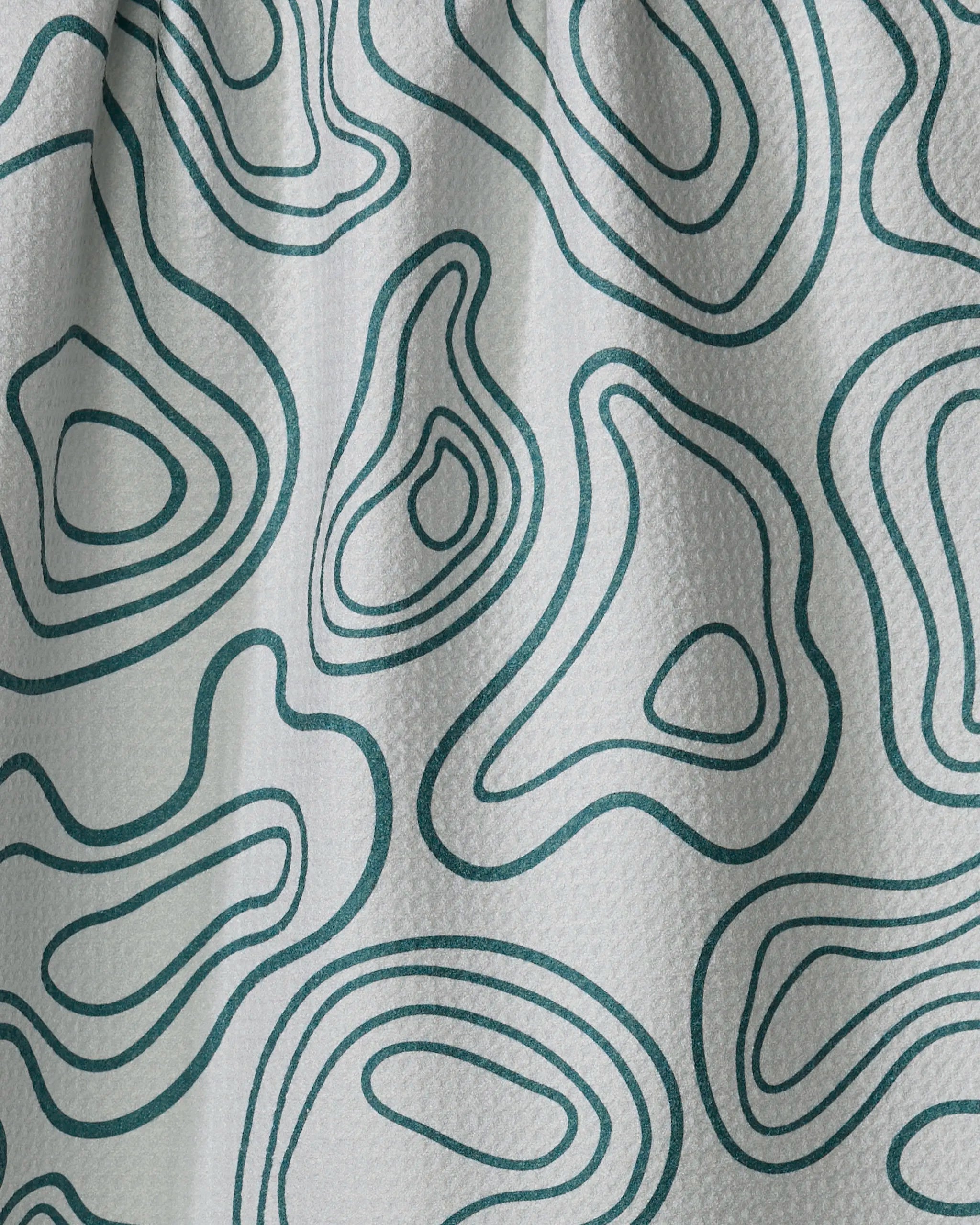 Close-up of Twig + Spark’s Depth Chart white textured fabric, featuring an abstract green contour line pattern inspired by topographic maps, flowing smoothly like a tea towel over the surface.