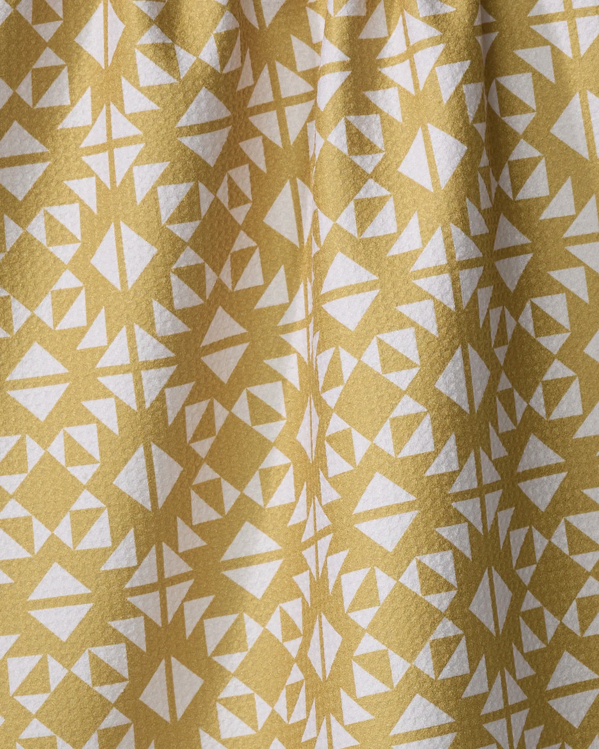 A close-up of Ash Cascade's Desert Geo towel shows yellow fabric with a repeating white geometric pattern of triangles and diamonds, slightly gathered at the top.