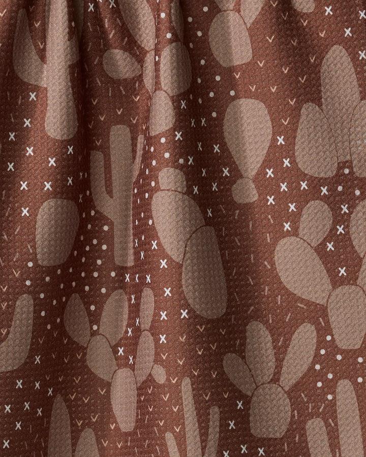 Desert Night by Rosa Kichline: a brown recycled fabric kitchen towel with a textured feel, featuring beige cacti and white X and dot patterns. Drapes beautifully with visible folds—eco-friendly style for your home.