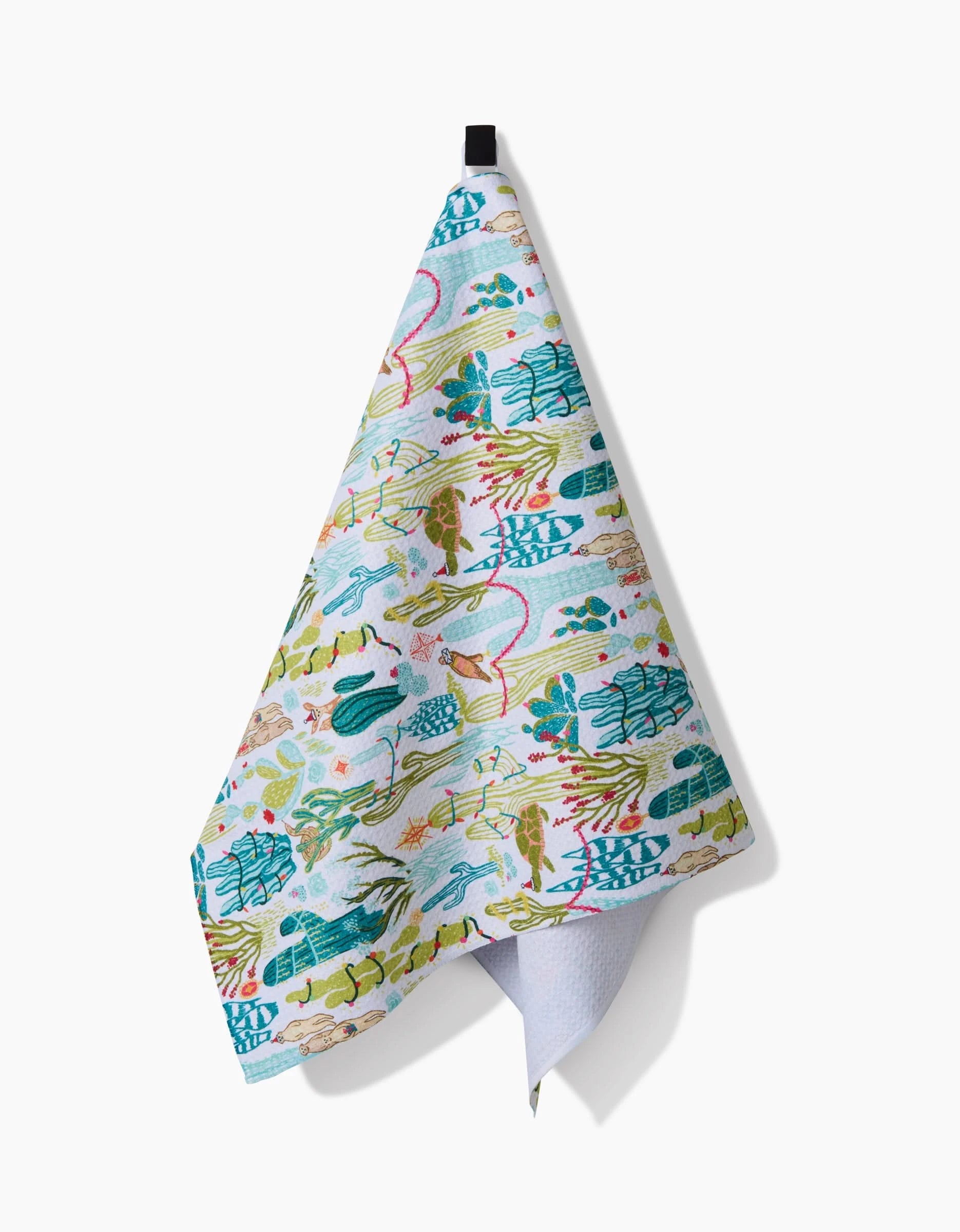 The Desert On Holiday kitchen towel by Elisabeth Wing, featuring a vibrant botanical and bird design, hangs from a black hook against a white background.