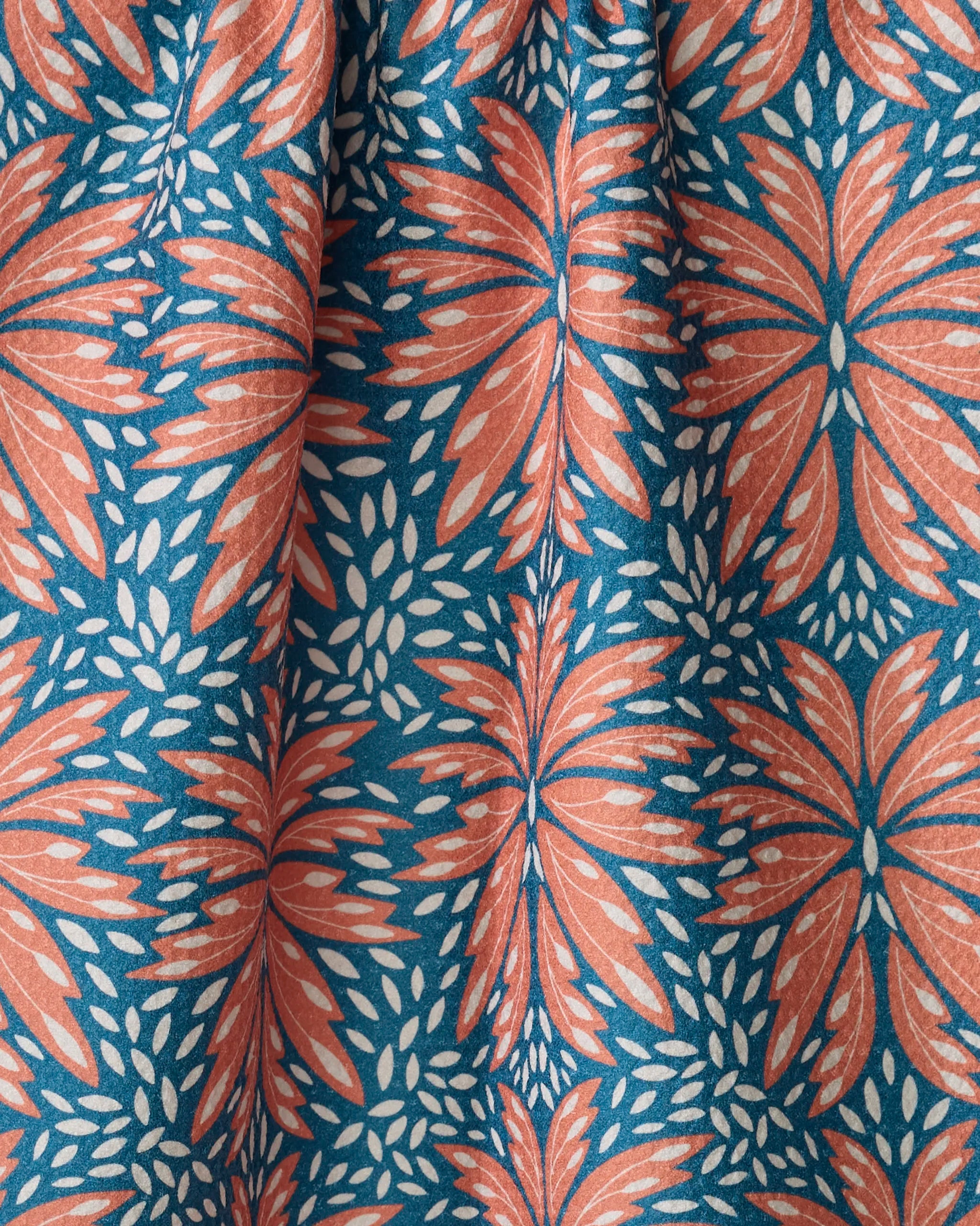 The Dew Drops fabric by Rebecca Woolbright features a bold coral orange and white floral pattern on deep blue, with large stylized petals and small leaf accents. Made from quick-drying recycled materials, it's slightly gathered for soft folds.