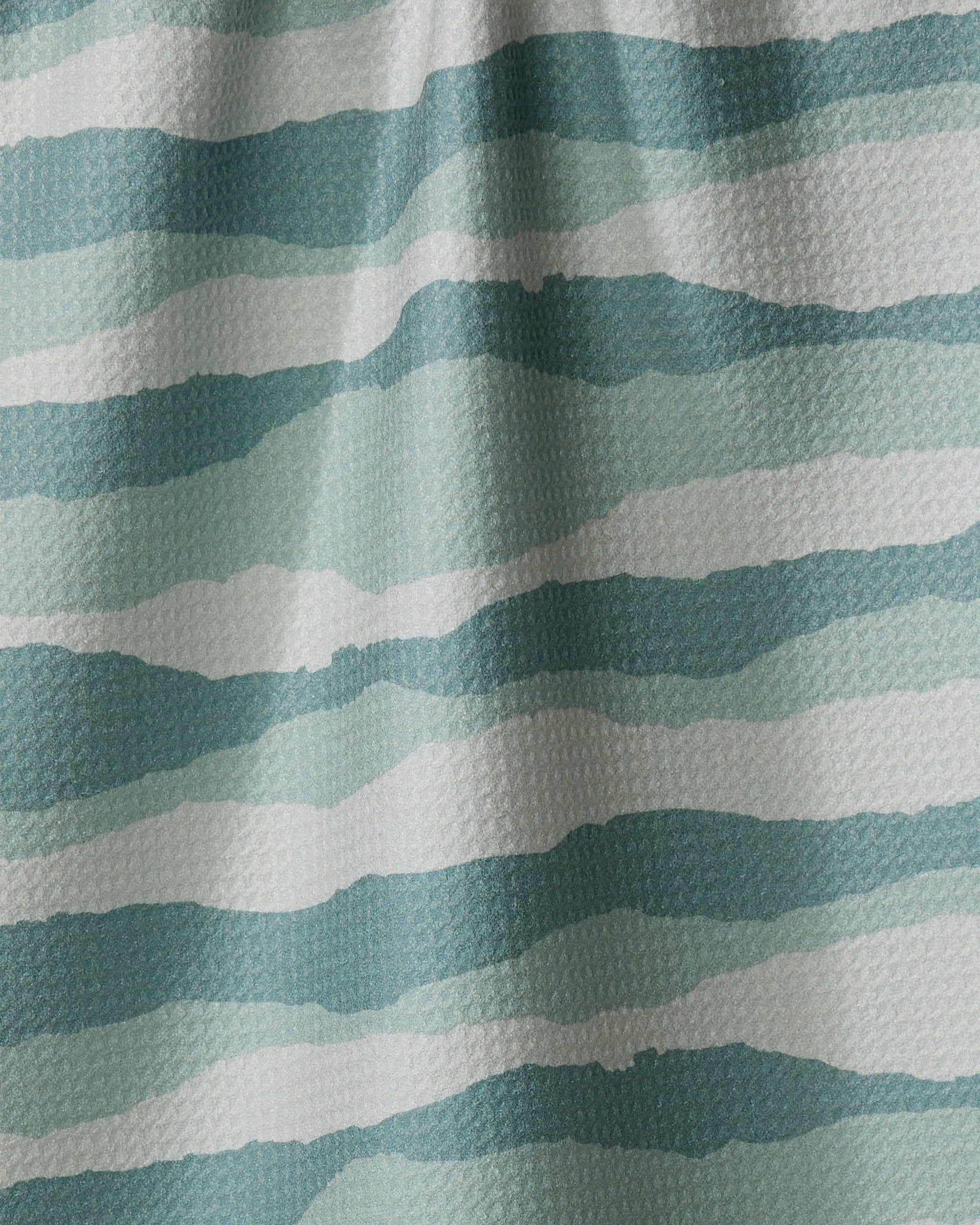 A close-up of Twig + Spark's Distant Landscape tea towel, made from recycled materials, with wavy blue and teal watercolor-effect stripes and a subtly textured fabric.