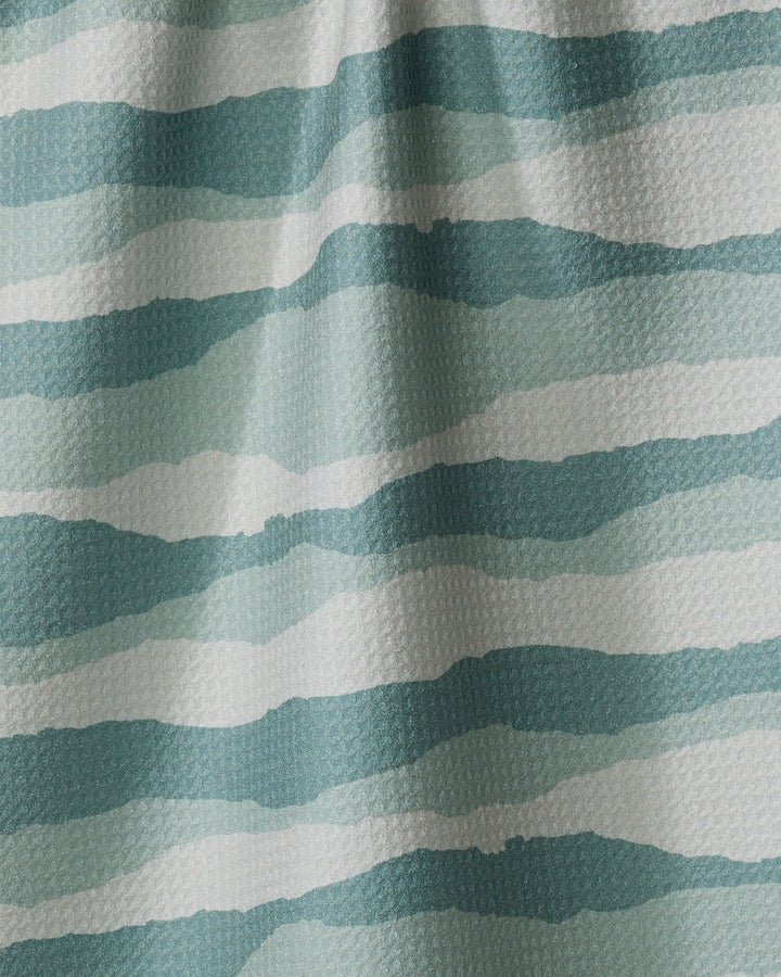 A close-up of Twig + Spark's Distant Landscape tea towel, made from recycled materials, with wavy blue and teal watercolor-effect stripes and a subtly textured fabric.