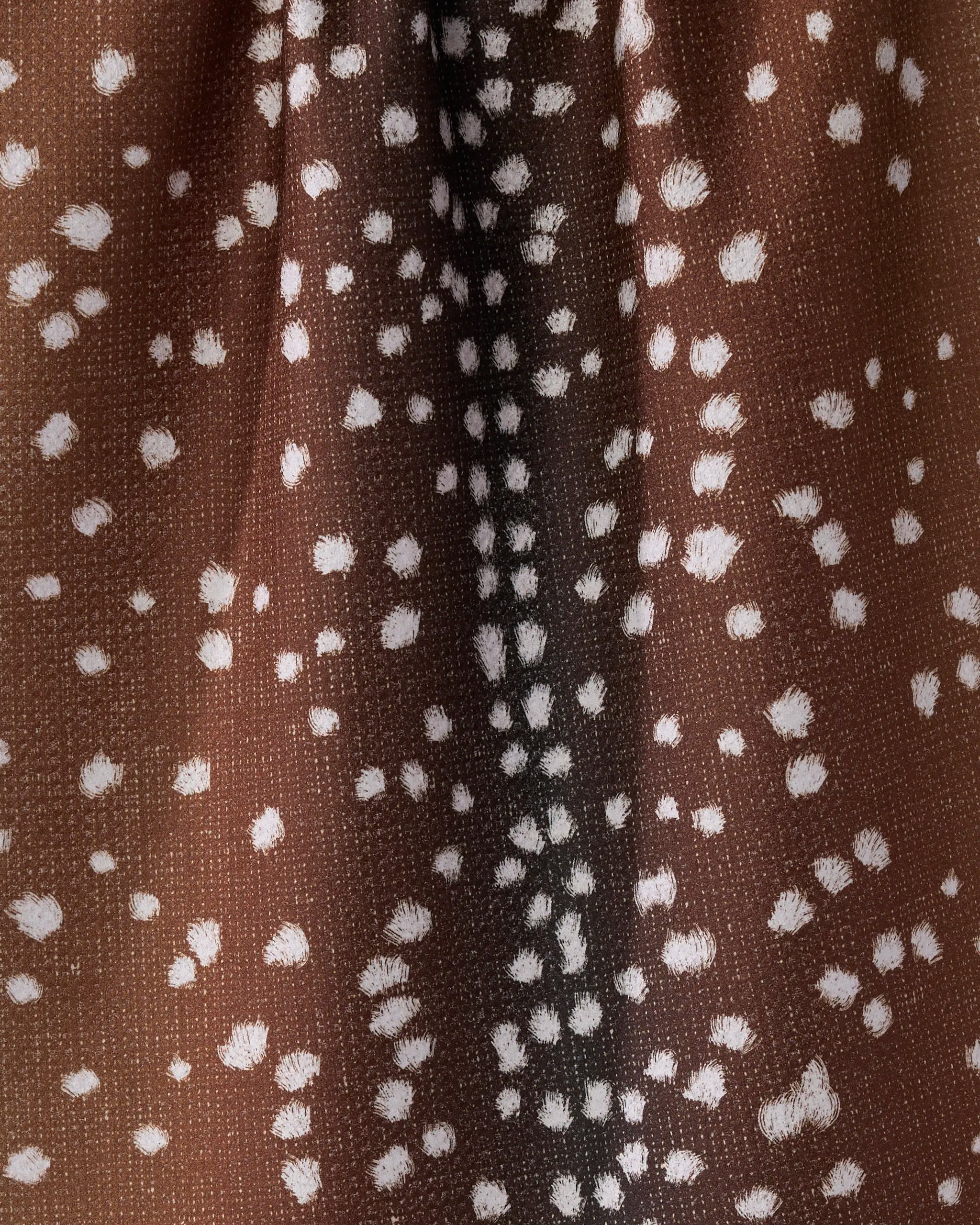 A close-up of Geometry’s Doe Trail tea towel, made from recycled materials. The ultra-absorbent towel features brown fabric with white spots and streaks, mimicking deer fur, and is shown gathered in textured folds.