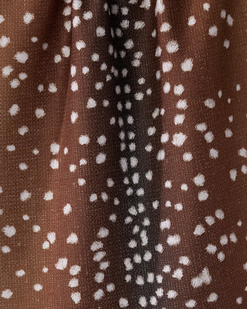 A close-up of Geometry’s Doe Trail tea towel, made from recycled materials. The ultra-absorbent towel features brown fabric with white spots and streaks, mimicking deer fur, and is shown gathered in textured folds.