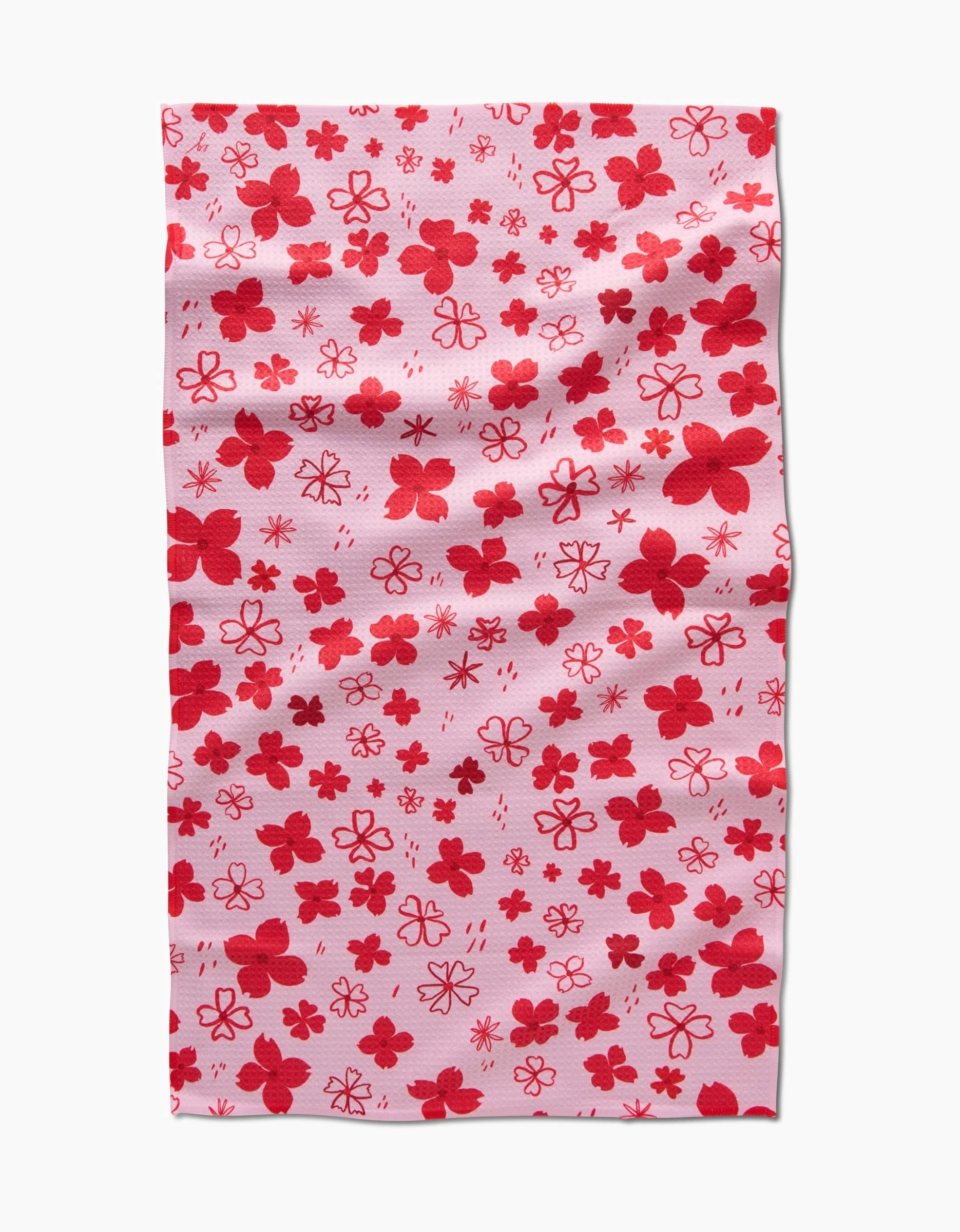 Dogwood Hearts by Elana Gabrielle is a rectangular pink tea towel with a scattered pattern of red and dark pink flowers.