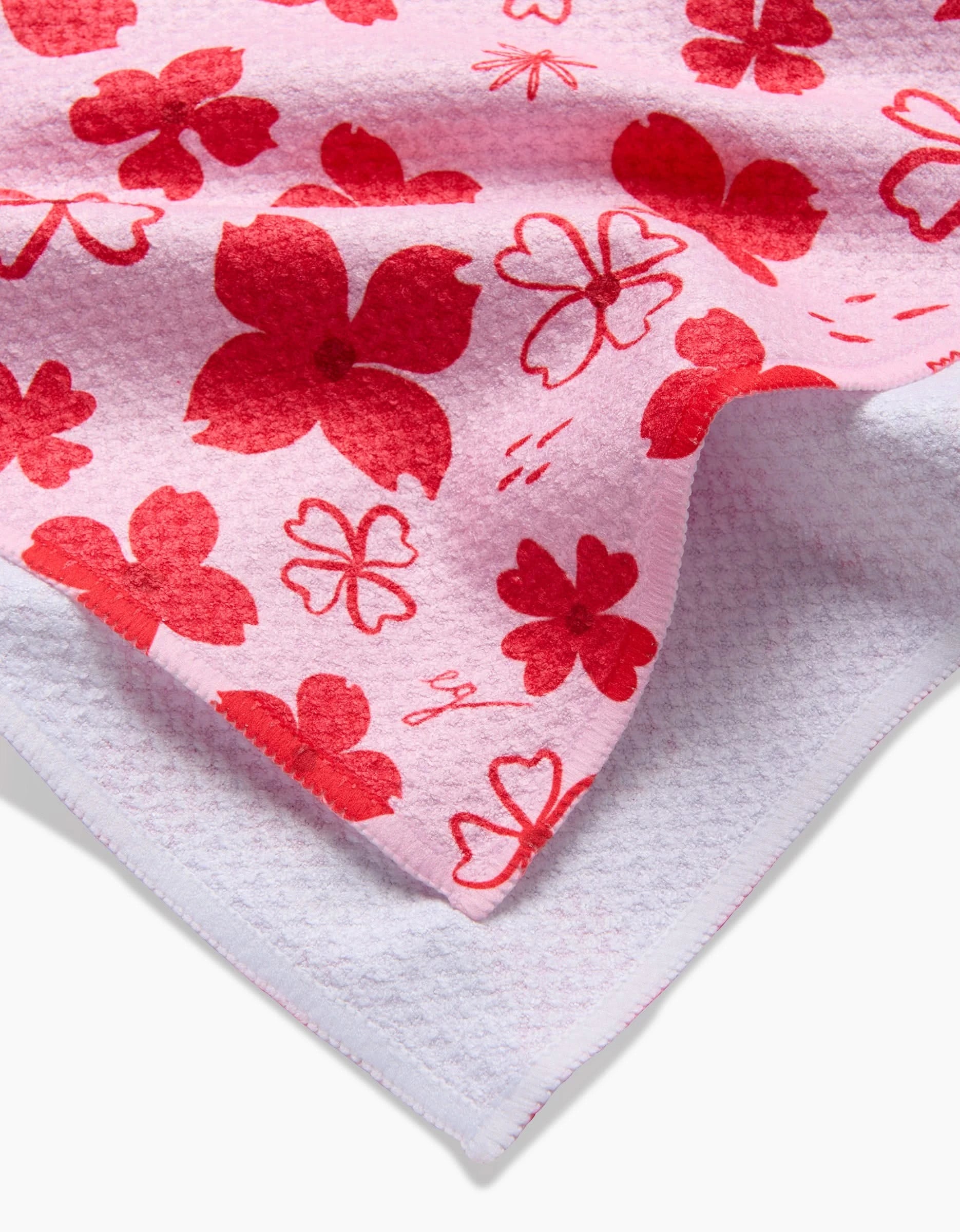 Dogwood Hearts by Elana Gabrielle is a pink textured quick-drying towel featuring red and pink floral patterns, folded at one corner to show its white underside.
