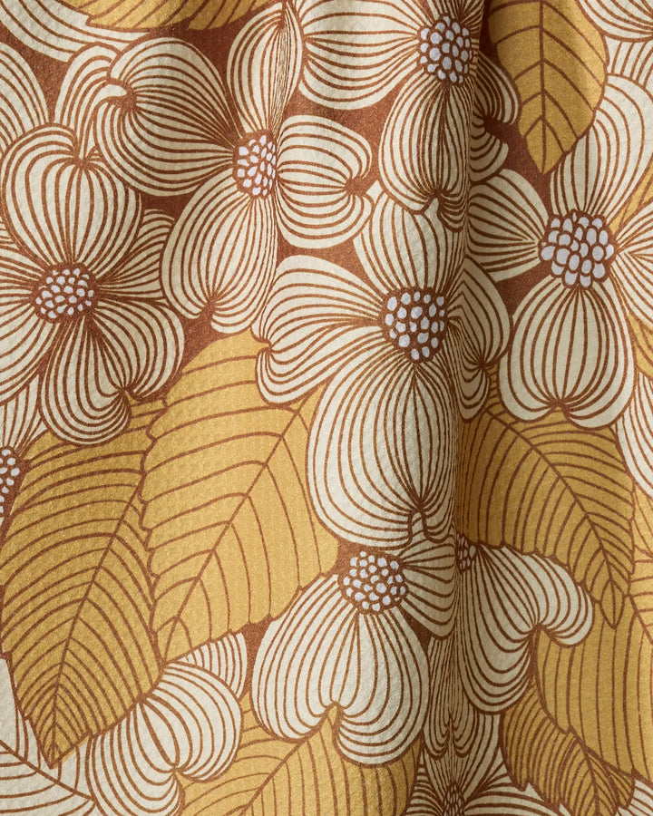 A close-up of the Dogwood tea towel by Katie O'Shea, featuring an ultra-absorbent fabric with a retro floral pattern of large cream dogwood flowers and yellow leaves outlined in brown on a textured background.