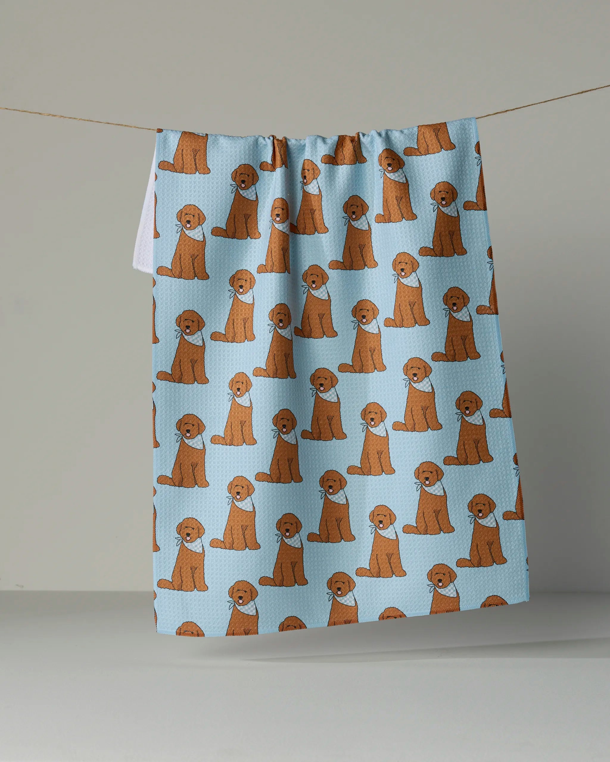 The Geometry Doodle Days kitchen tea towel is made from recycled materials and features a repeating pattern of cartoon brown dogs hanging on a line against a plain light blue background.