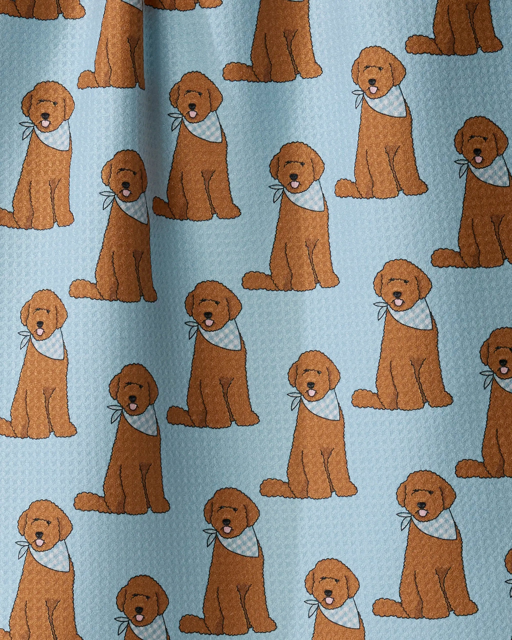 Introducing Doodle Days by Geometry—a kitchen tea towel crafted from recycled materials, featuring a light blue fabric adorned with a repeating pattern of cartoon brown dogs wearing matching light blue bandanas, all sitting in similar poses. The towel’s textured appearance, soft folds, and subtle shadows add extra charm to your kitchen décor.