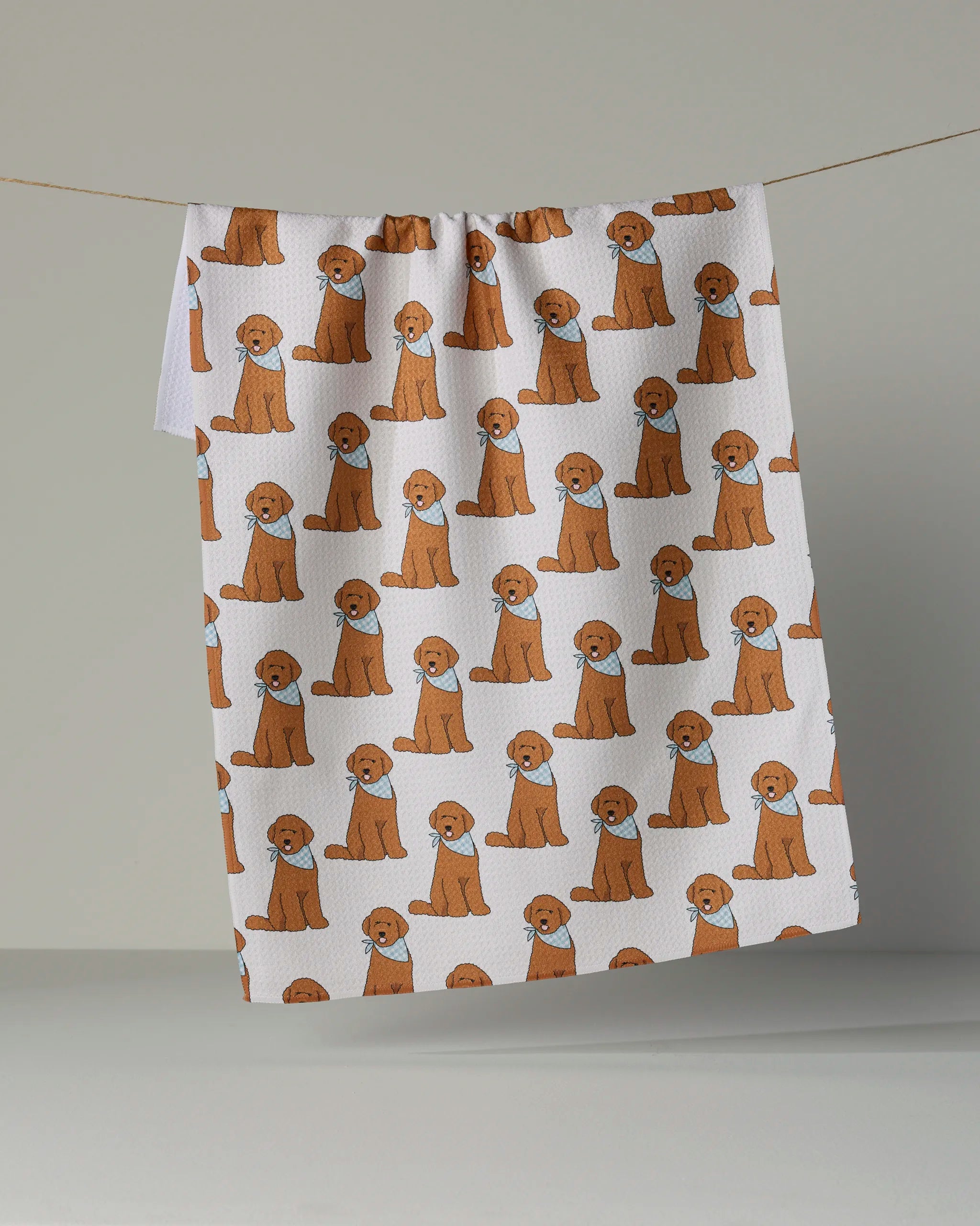 The Geometry Doodle Days tea towel features a repeating pattern of cartoon brown dogs on a white background and is shown hanging on a line against a plain backdrop. Made from recycled materials, this quick-drying towel adds both charm and sustainability to your daily routine.