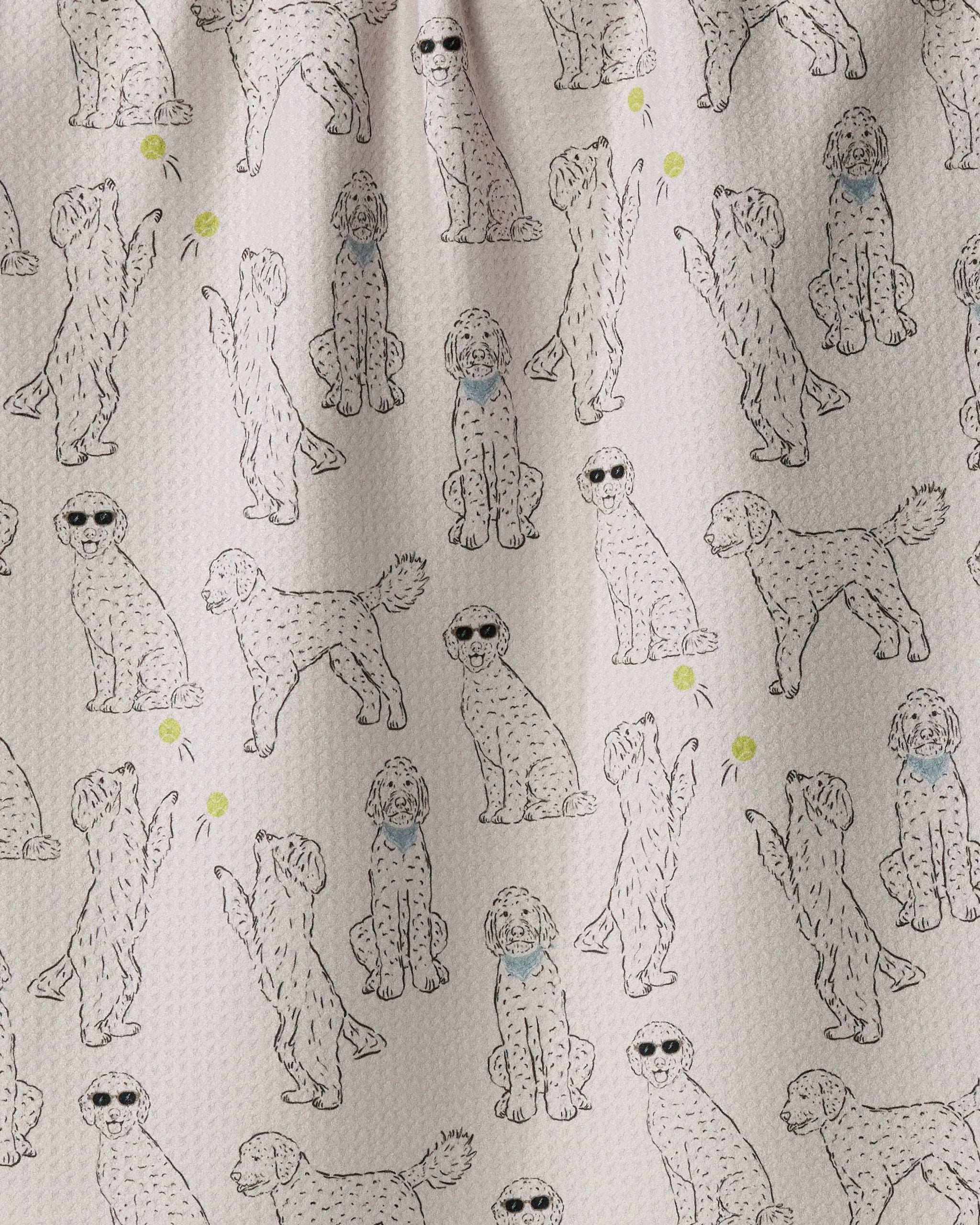 Introducing “Doodle Daze” by Geometry—a playful kitchen towel made from recycled materials, featuring a light textured background adorned with hand-drawn dogs in assorted poses (some sporting sunglasses or blue collars) and scattered yellow tennis balls.