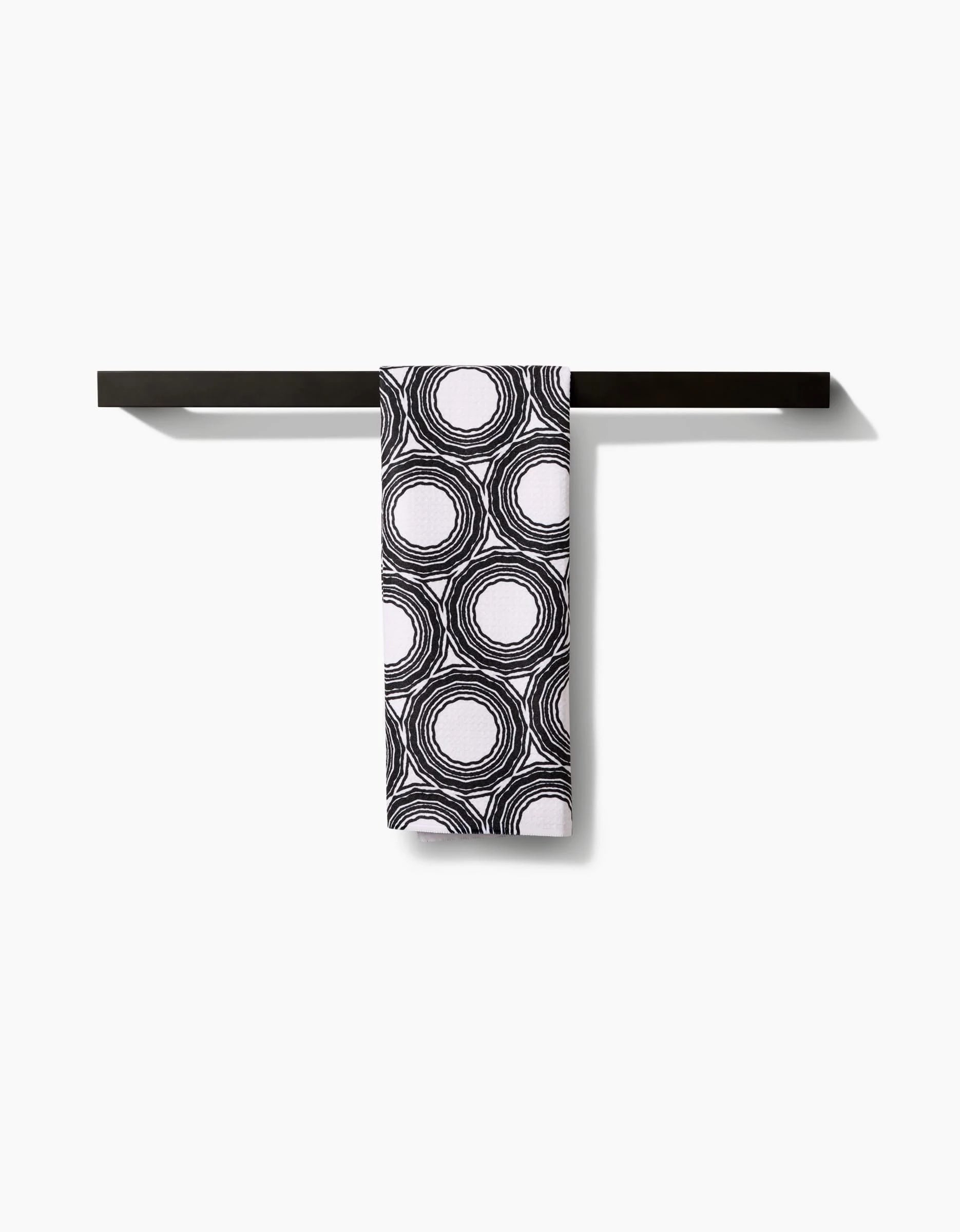 The Katherine Berkeley Dosido tea towel, featuring a black and white circular pattern, is neatly draped over a simple black towel bar against a plain white background.