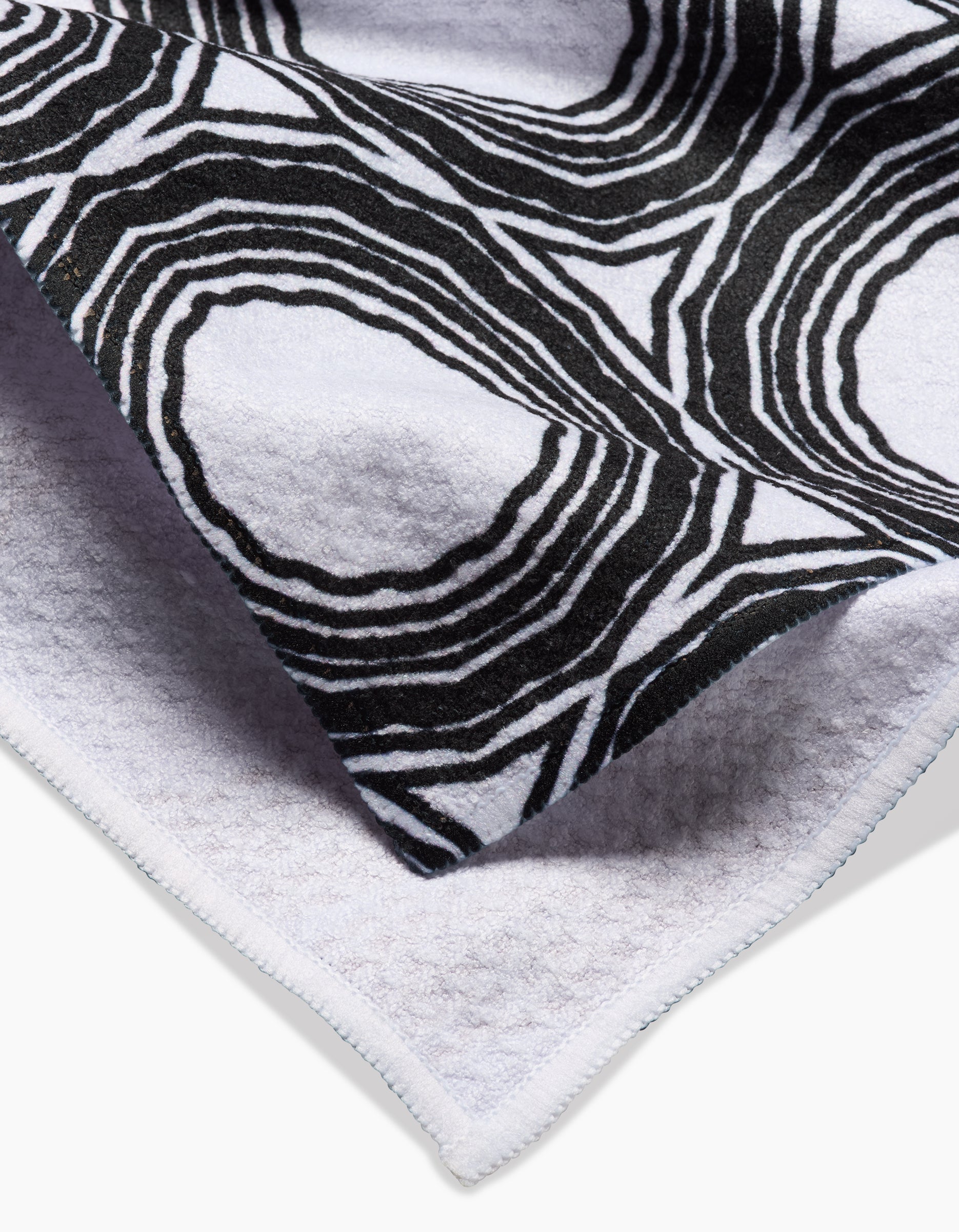 A close-up of the Dosido tea towel by Katherine Berkeley, showing its folded white Geoweave fabric with a black abstract circular line pattern on one side and a plain textured surface on the other.