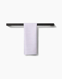 The Geometry Dot Dot Dot Blushed Bergamot towel, ultra-absorbent and white, is neatly draped over a minimalist black towel rack on a white wall, casting a subtle shadow to the right.